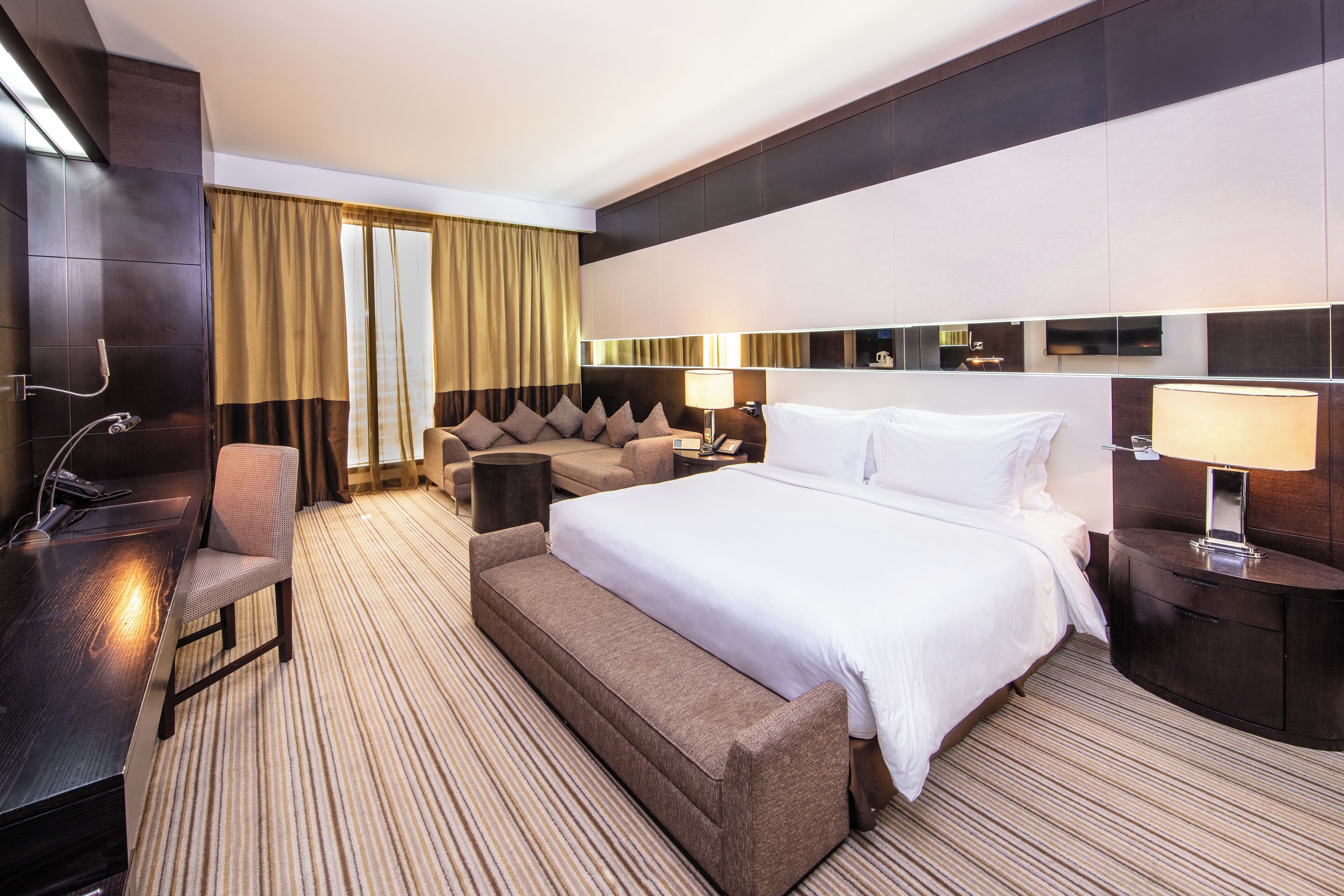 A modern hotel room with a large bed, a sofa, a desk, and a TV.