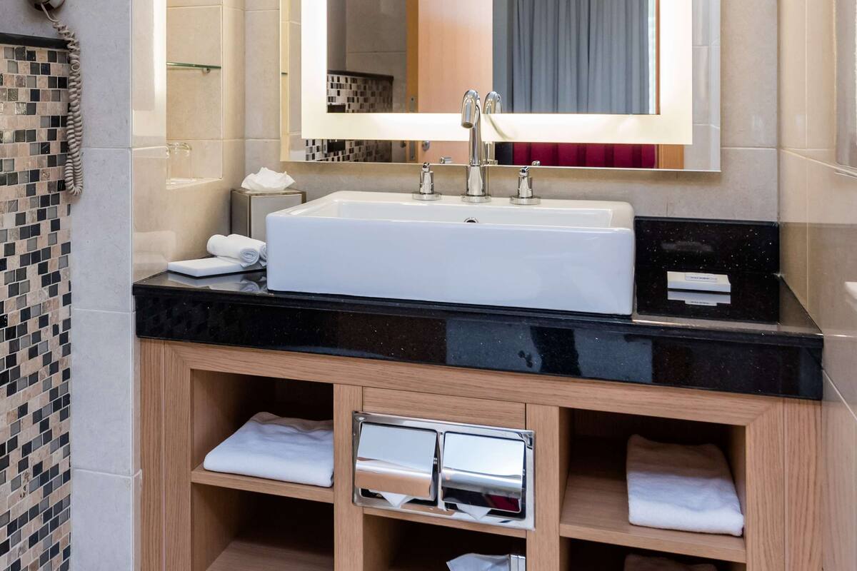 A modern bathroom with a large mirror, white sink, and wooden vanity.