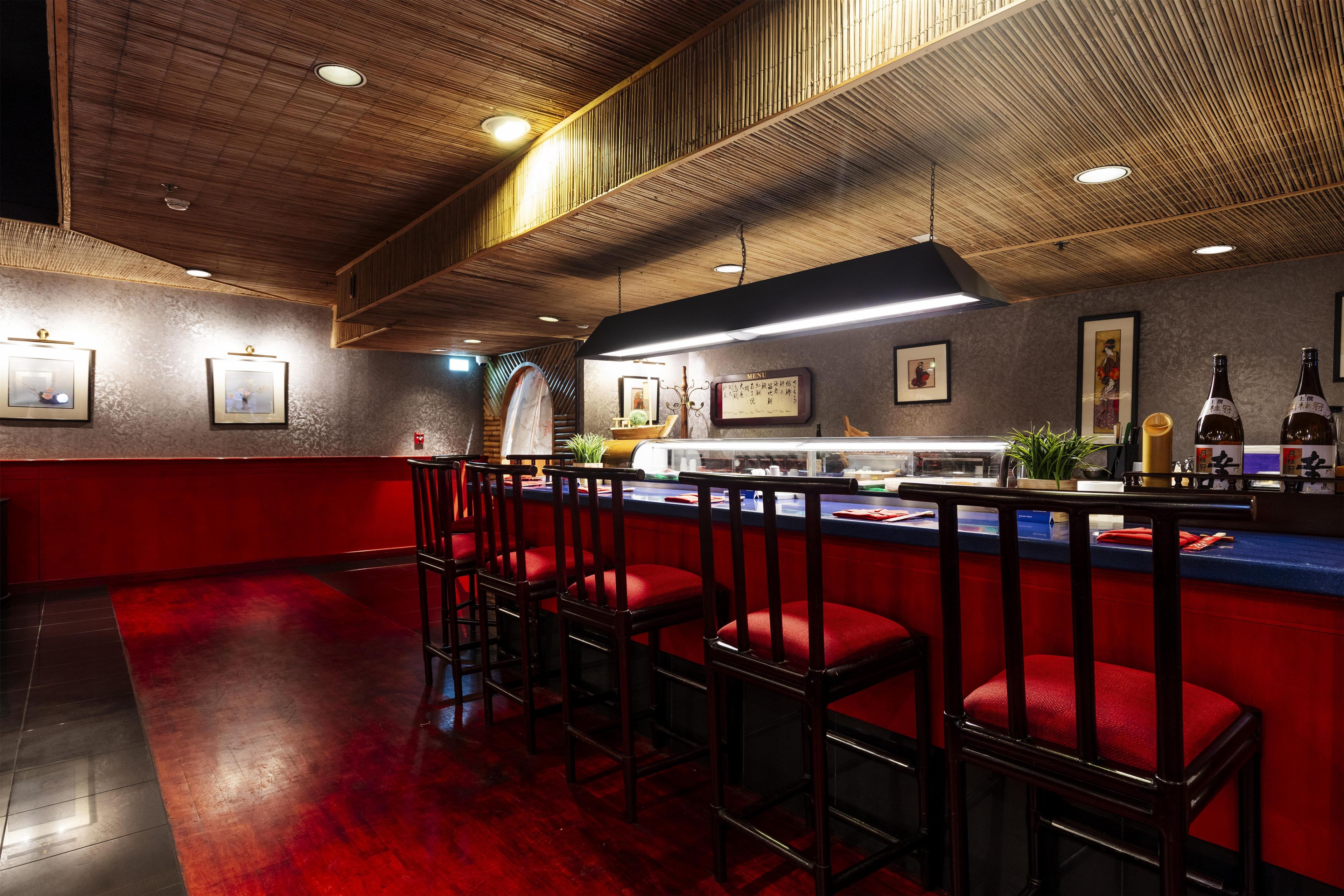 L’intérieur d’un restaurant, avec un bar, des tabourets de bar rouges et un panneau affichant le menu.