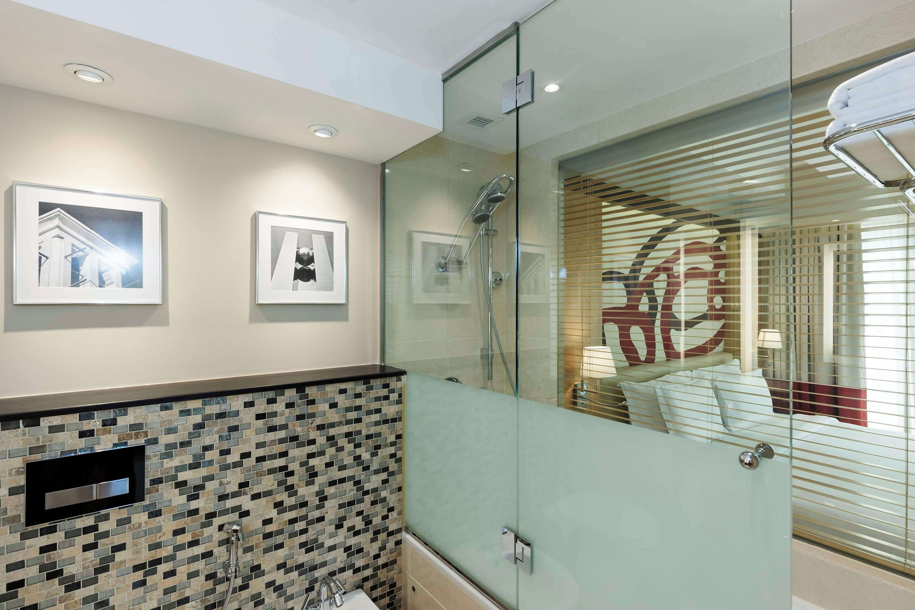 A modern bathroom with a glass shower enclosure, a tiled backsplash, and framed pictures on the wall.