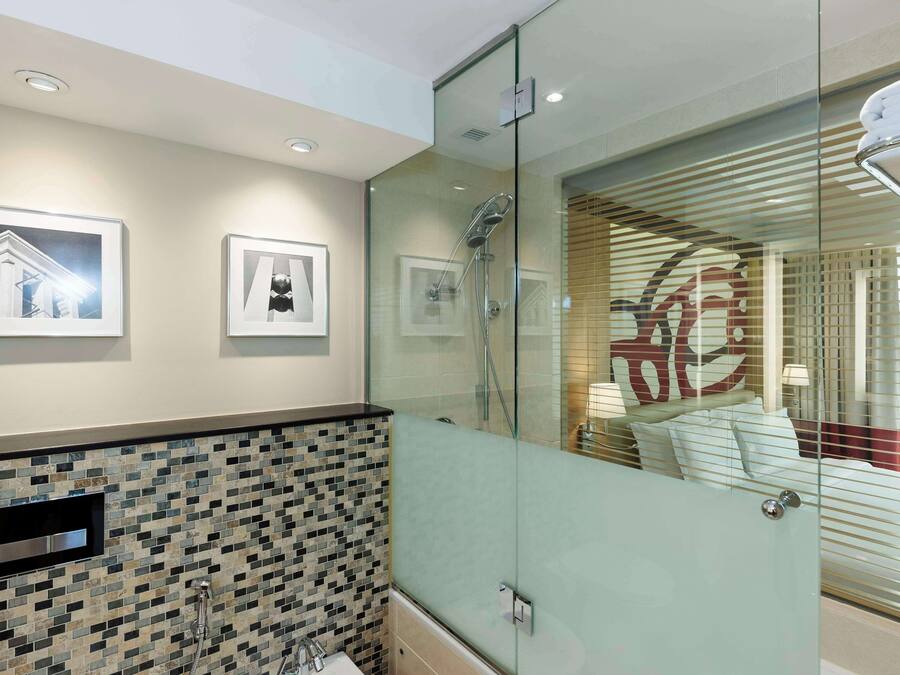A modern bathroom with a glass shower enclosure, a tiled backsplash, and framed pictures on the wall.