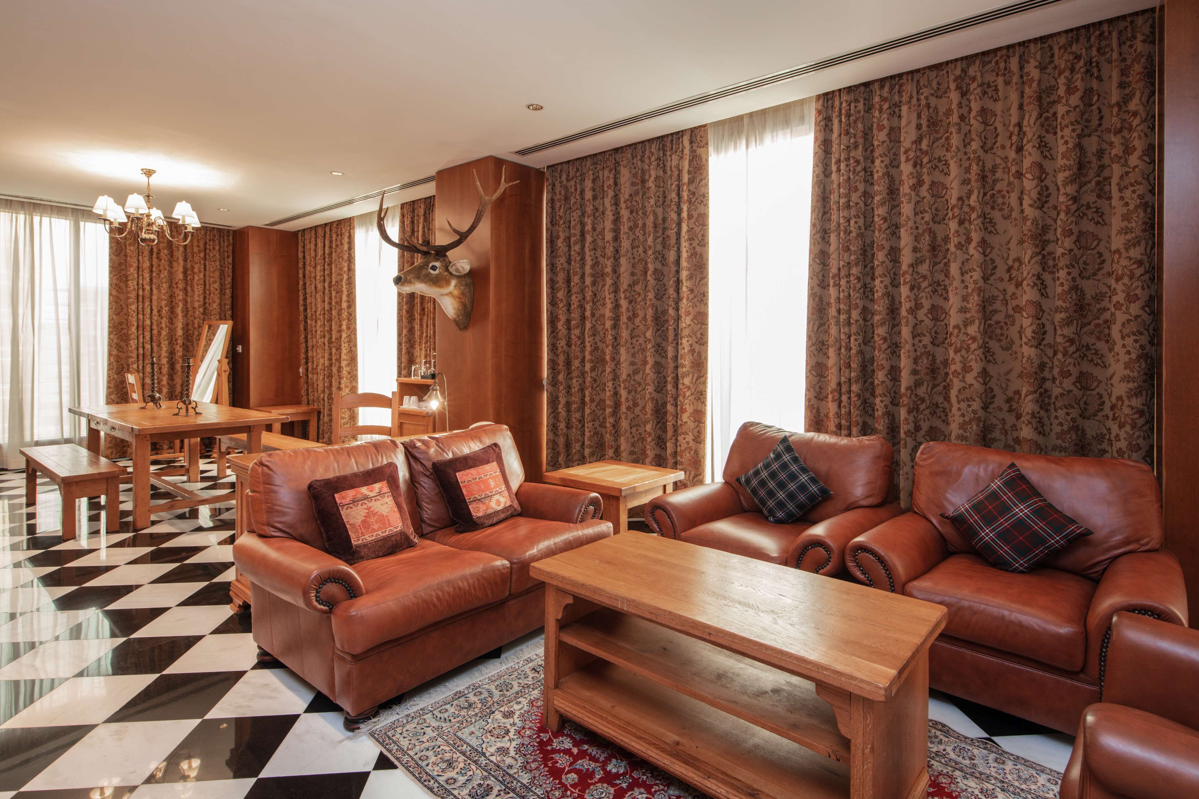 Uma sala de estar ampla com sofás de couro, uma mesa de centro de madeira e um candelabro.