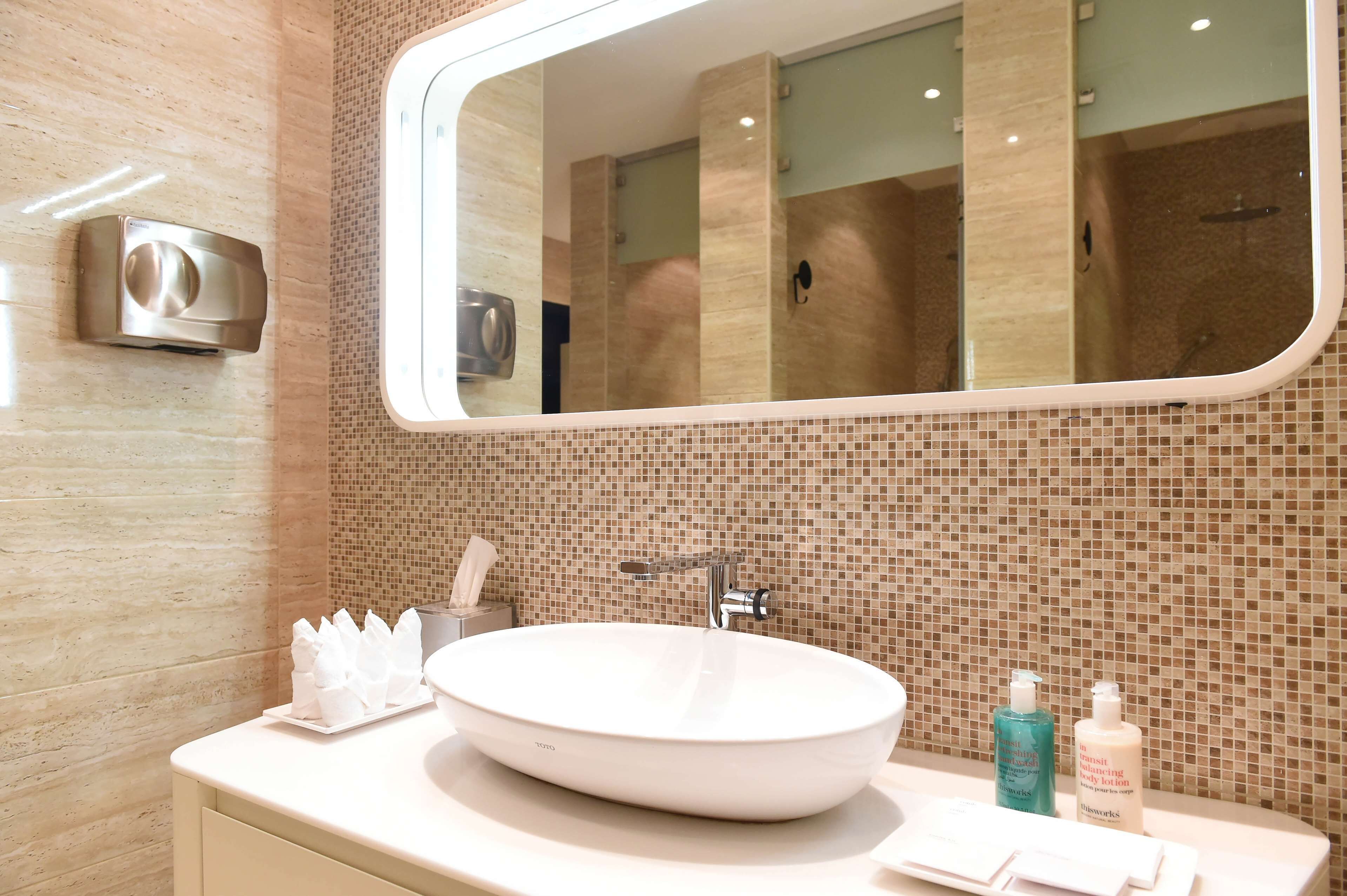 A bathroom with a large mirror, a white sink, and a tiled wall.