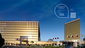 A Radisson hotel with a modern glass facade, multiple flags, and a clear sky.