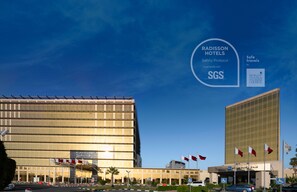 A Radisson hotel with a modern glass facade, multiple flags, and a clear sky.