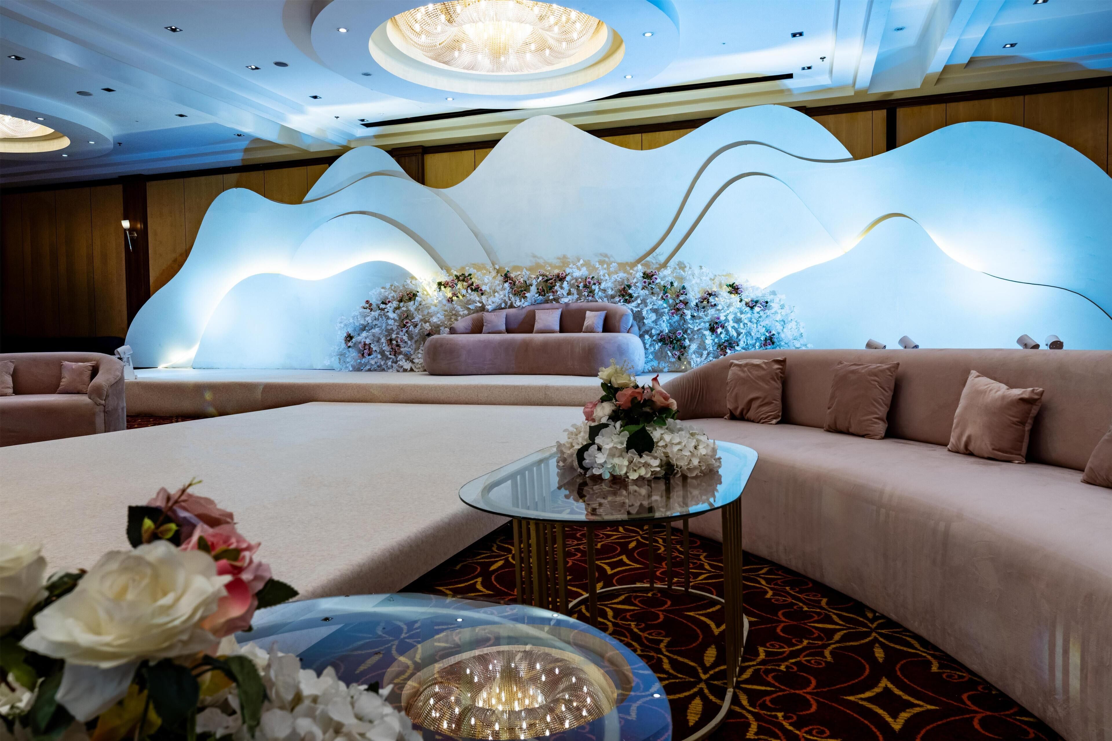 A modern hotel room with a curved sofa, a glass coffee table, and a decorative wall with floral arrangements.