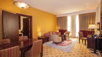 A hotel room with a dining area, a sofa set, a large mirror, and a red and white patterned rug.