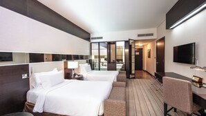 A hotel room with two beds, a desk, a chair, a TV, and a bathroom visible through an open door.