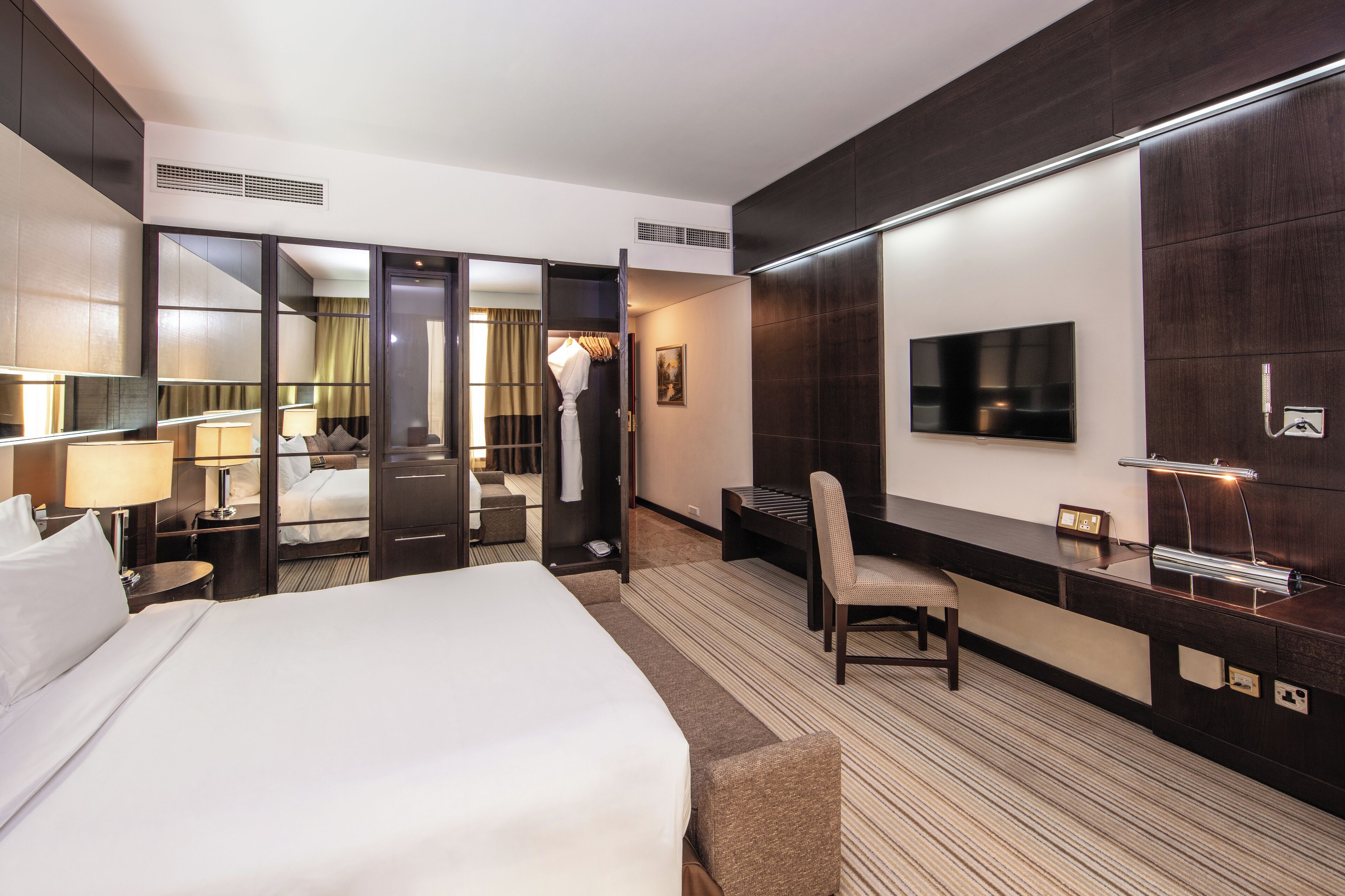 A hotel room with a large bed, a desk with a chair, a TV, and a mirror.