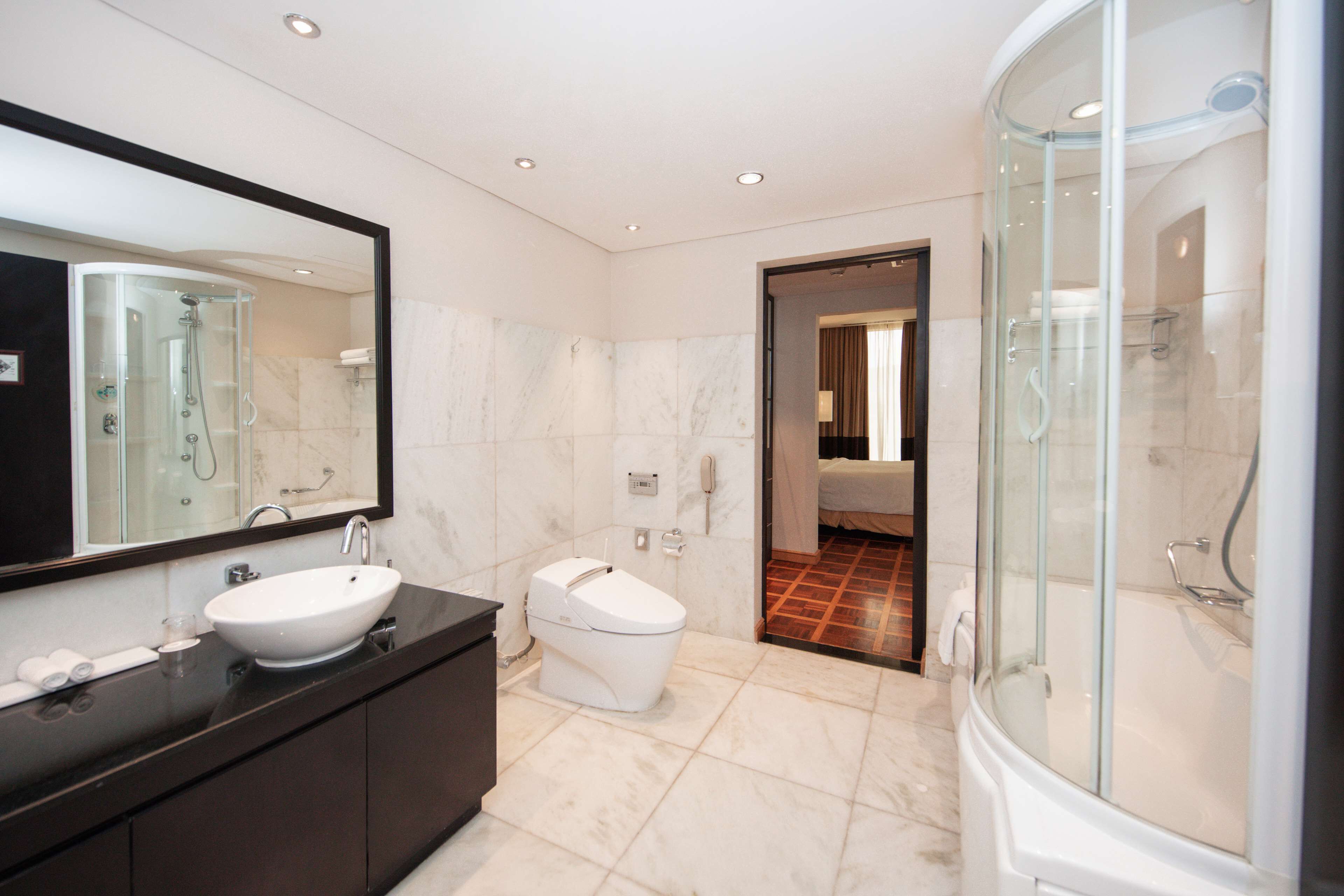 A modern bathroom with a large mirror, a sink, a toilet, and a glass-enclosed shower area.