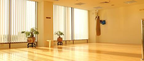 A spacious room with wooden flooring, large windows with blinds, and two potted plants.