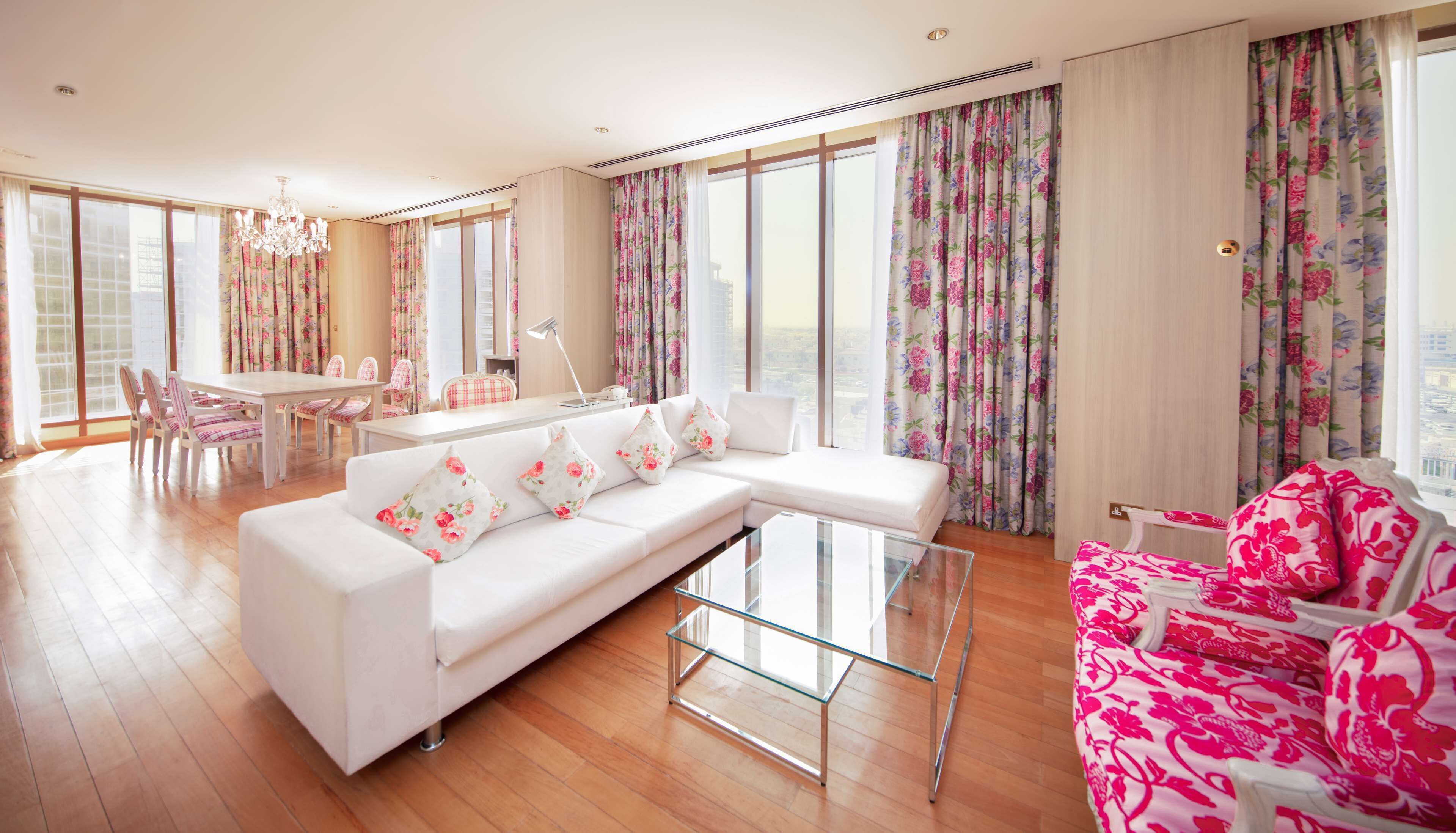 Un salón amplio con un sofá blanco, una mesa de centro de vidrio y cortinas con motivos florales.