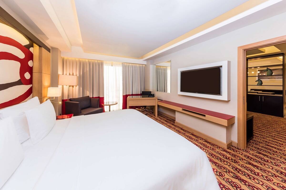 A hotel room with a large bed, a desk, a TV, and a wardrobe.