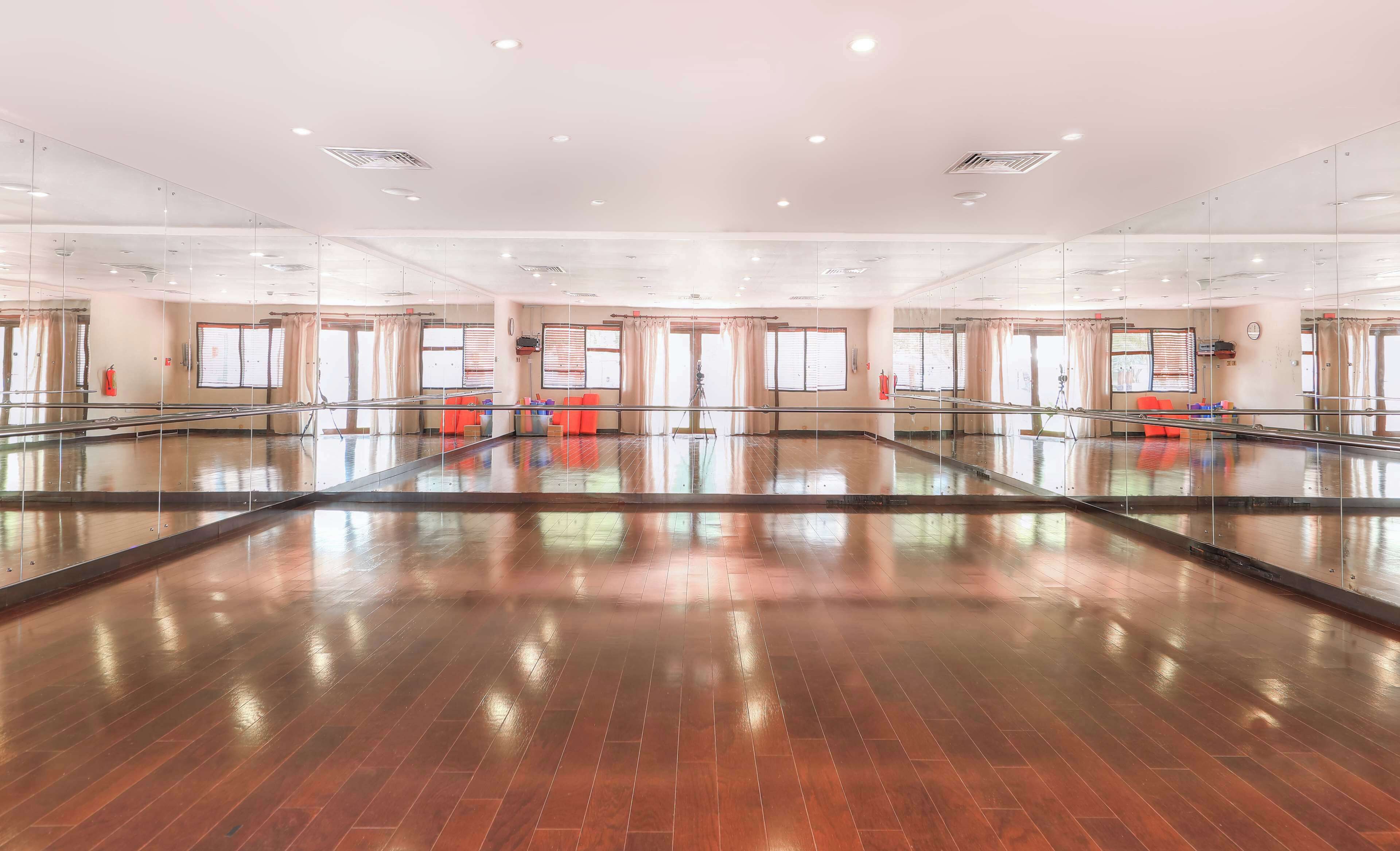 A spacious dance studio with a polished wooden floor, large mirrors, and a ballet barre.