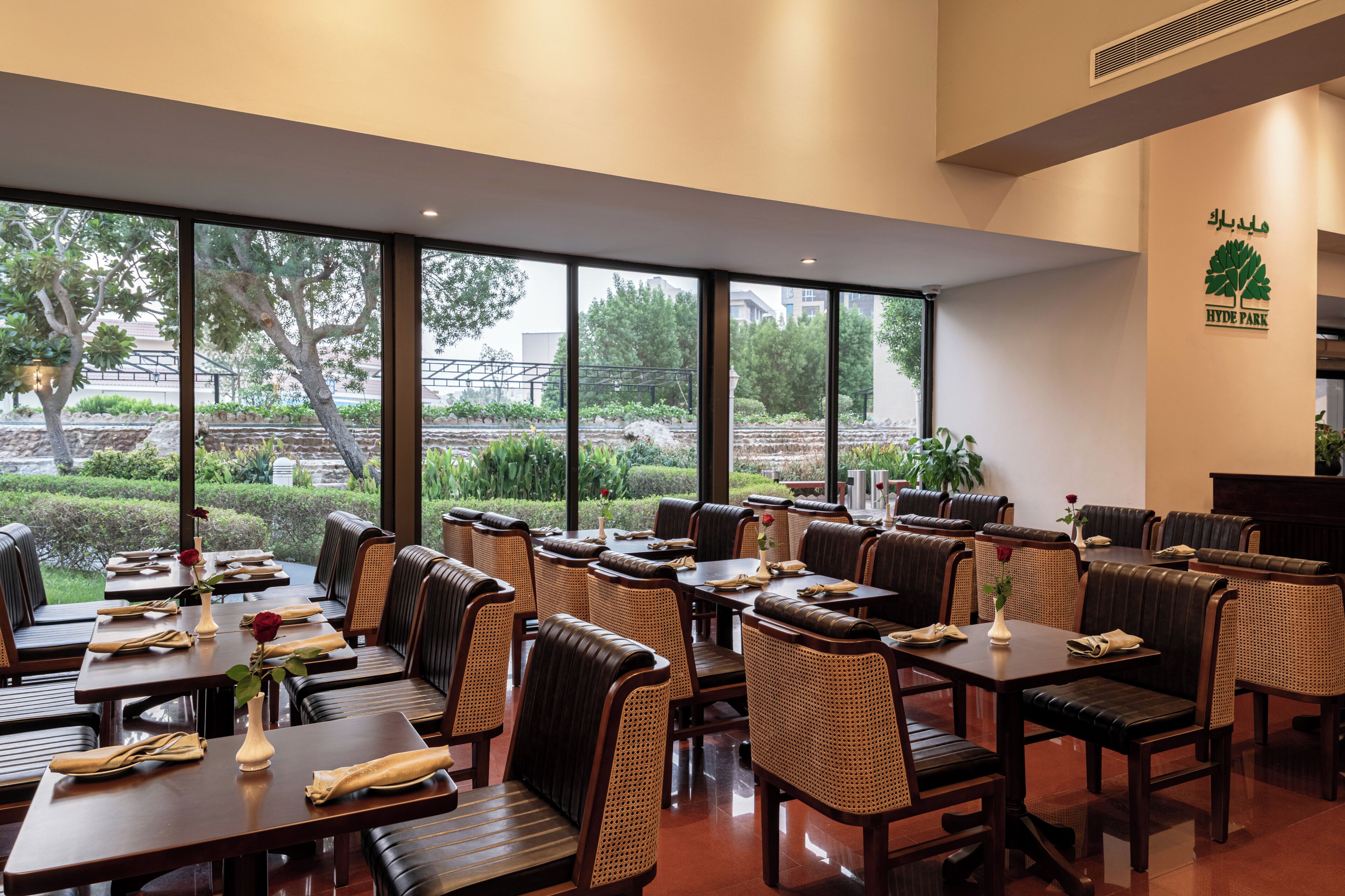 Un restaurante con mesas y sillas, amplias ventanas y vista a zonas verdes.