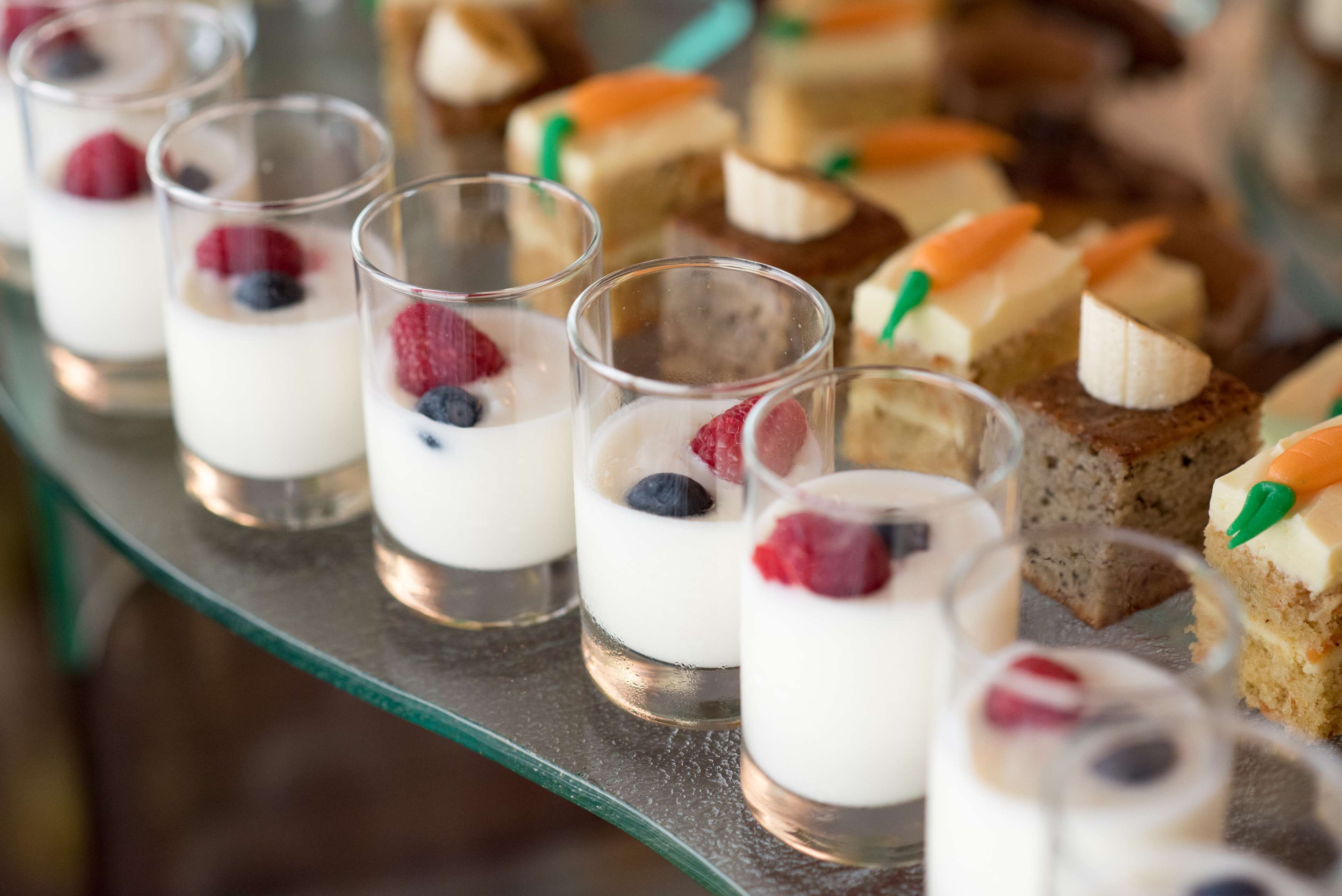 Una presentación de postres con vasitos de yogur coronados con bayas y diferentes pasteles.