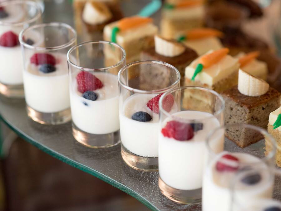 Una presentación de postres con vasitos de yogur coronados con bayas y diferentes pasteles.