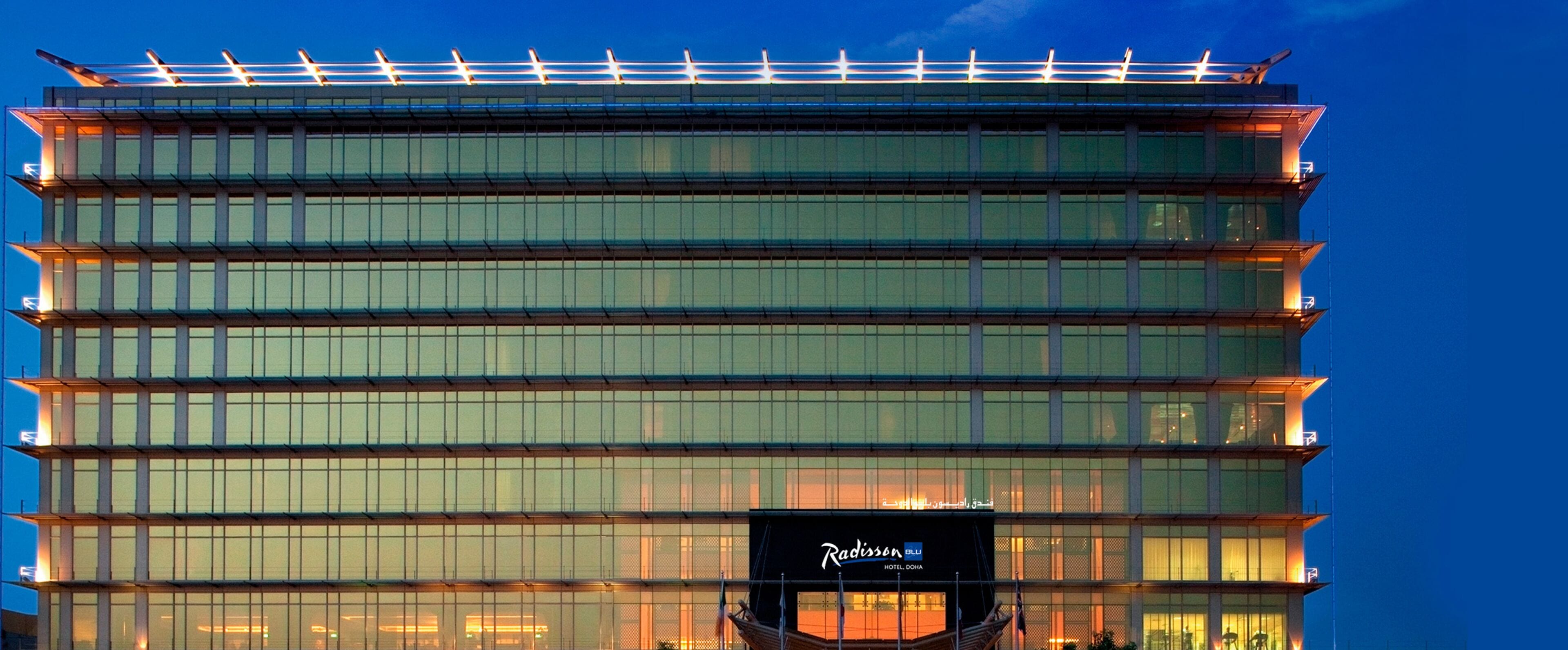 A multi-story hotel with a modern glass facade and a rooftop terrace.