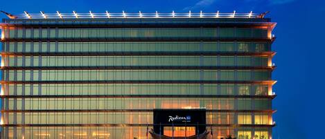 A multi-story hotel with a modern glass facade and a rooftop terrace.