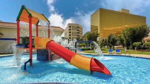 A water park with a red and yellow slide, a pool, and a modern building in the background.