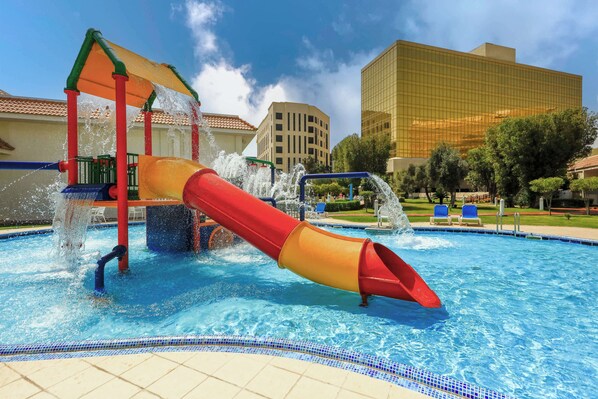 A water park with a red and yellow slide, a pool, and a modern building in the background.
