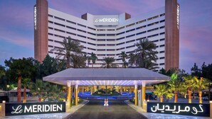 Un hotel de diseño moderno, con un llamativo letrero de 'Le Meridien', un acceso cubierto y un área ajardinada con palmeras.