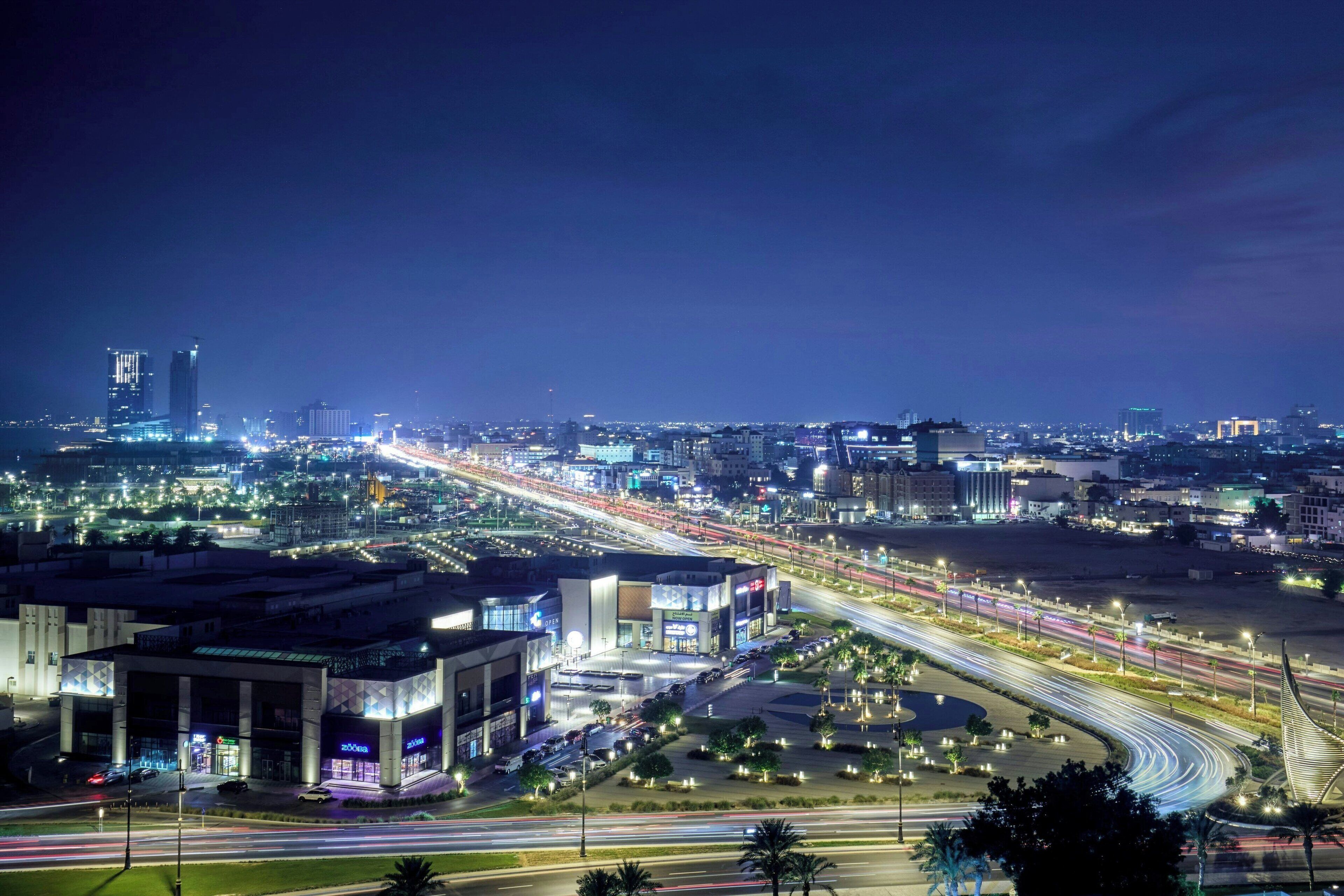 A nighttime cityscape with illuminated buildings, a curved road, and a modern bridge.