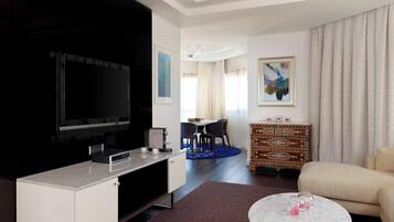 Una habitación de hotel moderna con televisor de pantalla plana, un área de comedor con mesa y sillas, un sofá, un aparador estampado y una araña.
