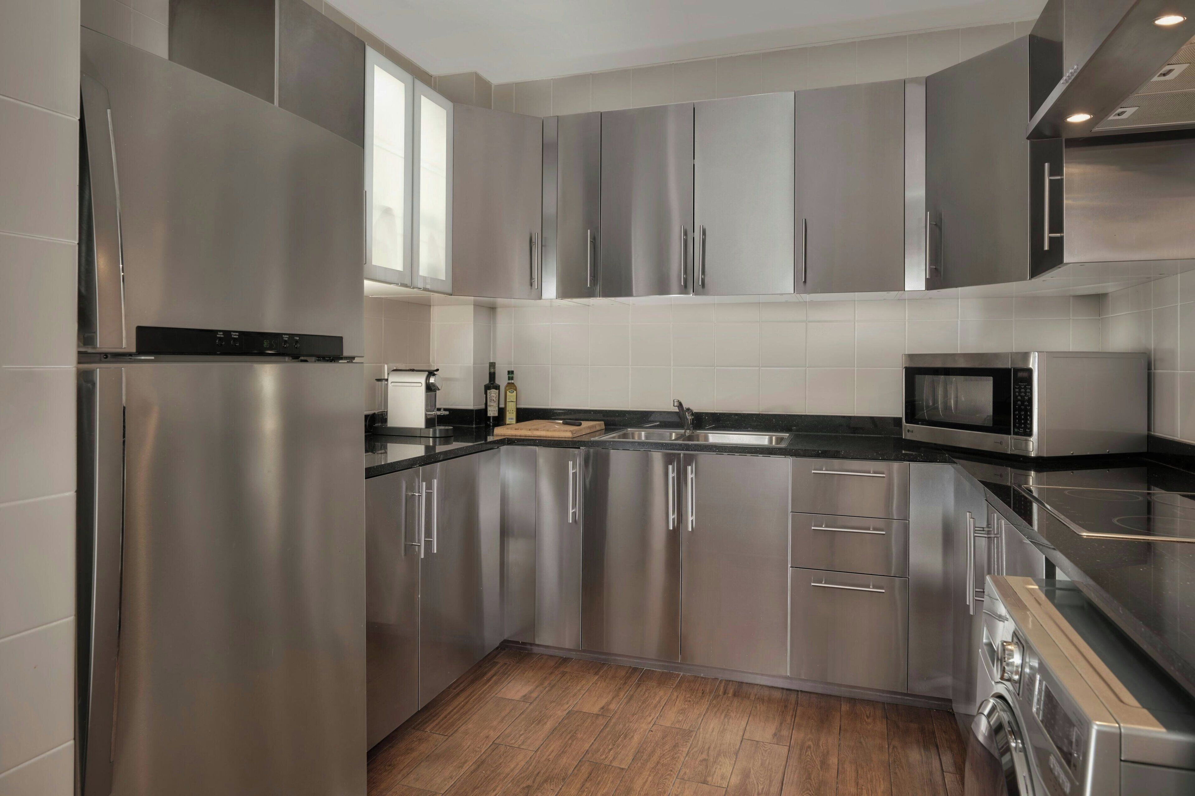 A modern kitchen with stainless steel appliances, a black countertop, and wooden flooring.