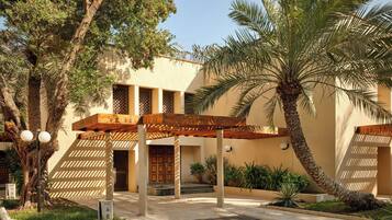 A building with a covered entrance, palm trees, and a clear sky.