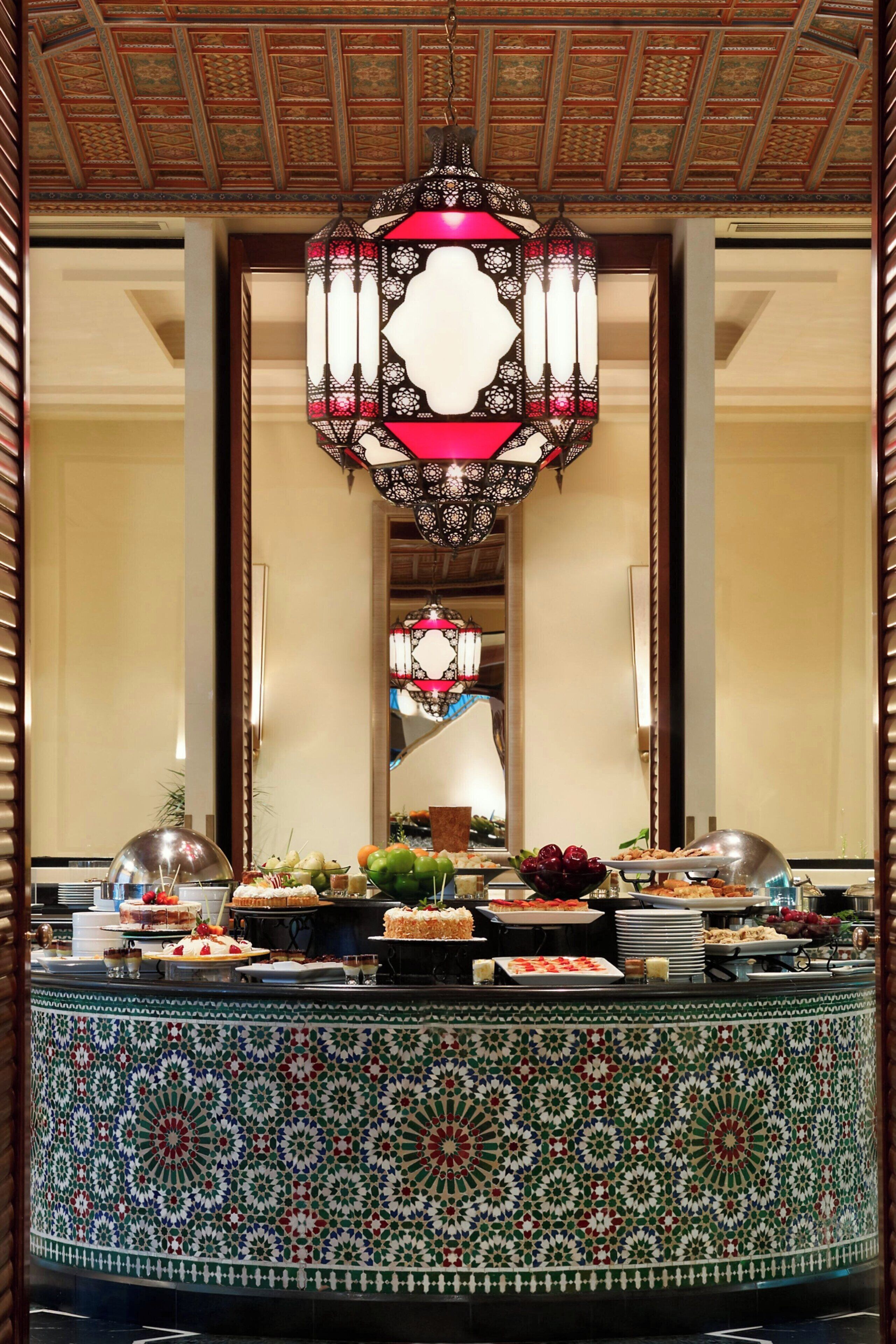 A buffet setup with a decorative hanging light fixture and a tiled wall with intricate patterns.
