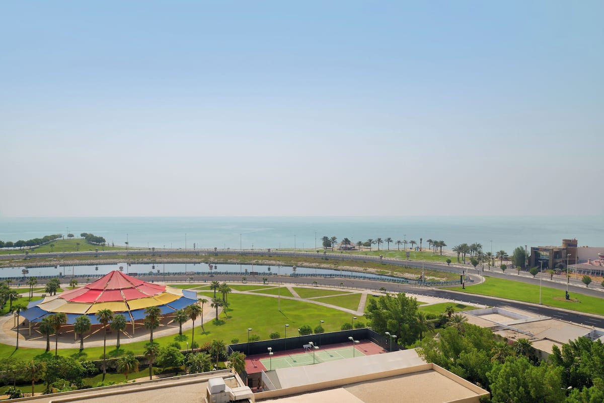 A view of a coastal area with a large red and yellow tent, a green lawn, and a road leading to a body of water.