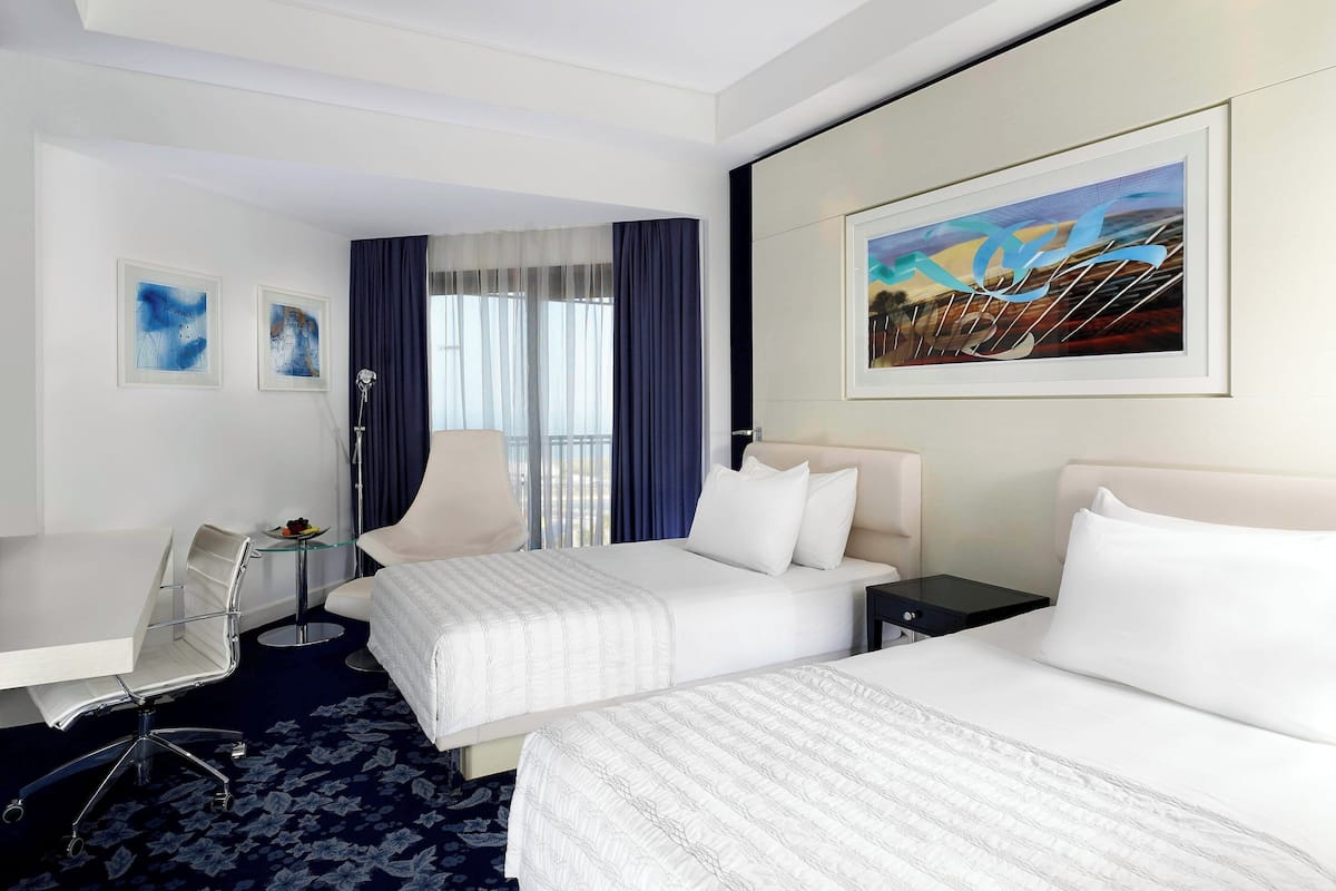 A hotel room with two beds, a desk, a chair, and a large window with curtains.