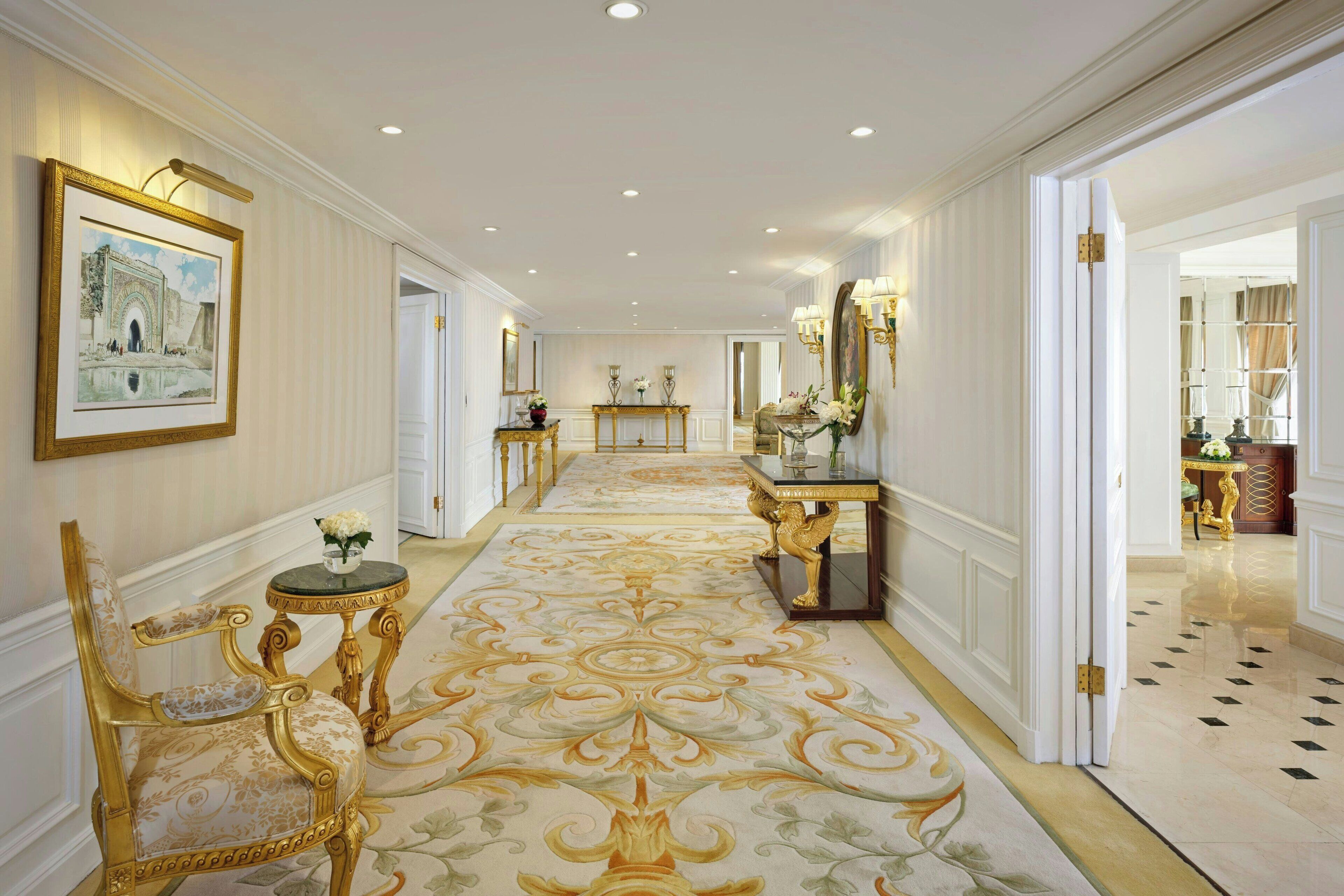 Un hall imponente con muebles dorados ornamentados, una alfombra estampada y un cuadro grande en la pared.