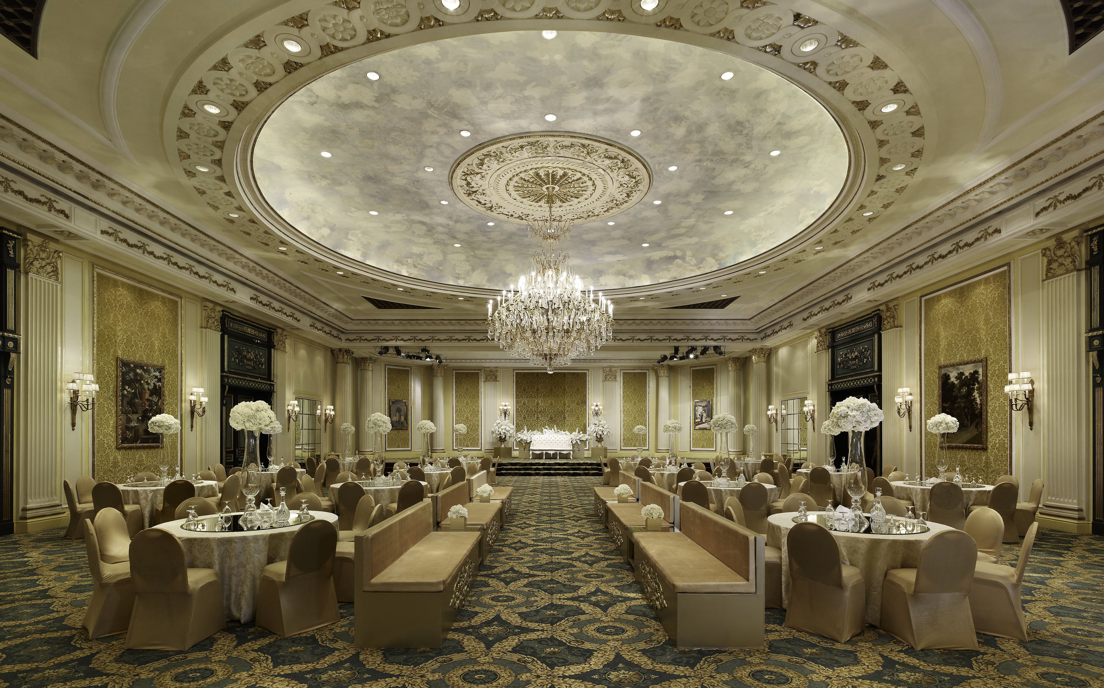 Ein prächtiger Ballsaal mit aufwendigen Kronleuchtern, stilvollem Tischgedeck und einem luxuriösen Teppich.