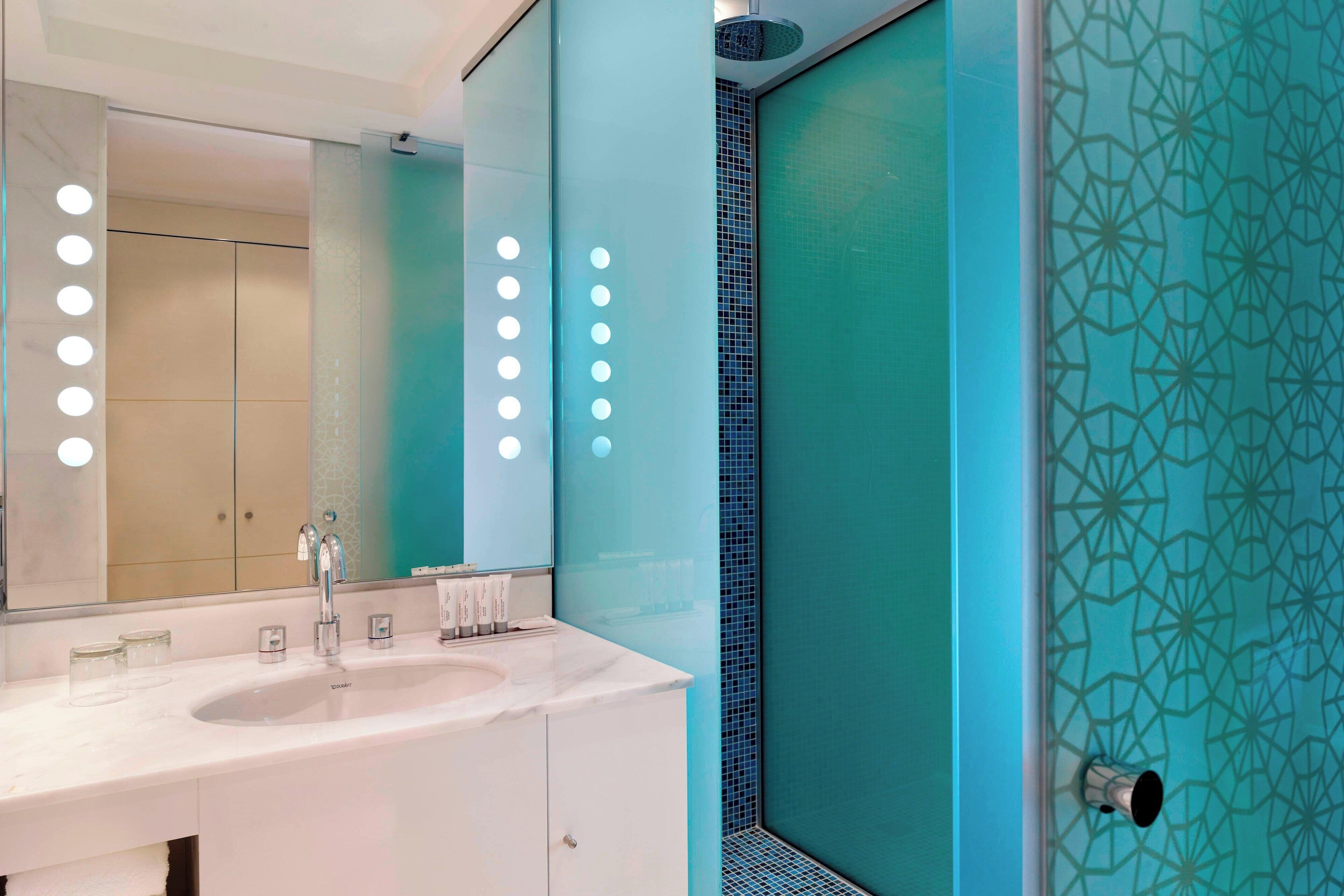 Een moderne badkamer met een wit wastafelmeubel, een grote spiegel en een douchegedeelte betegeld met blauwe tegels.