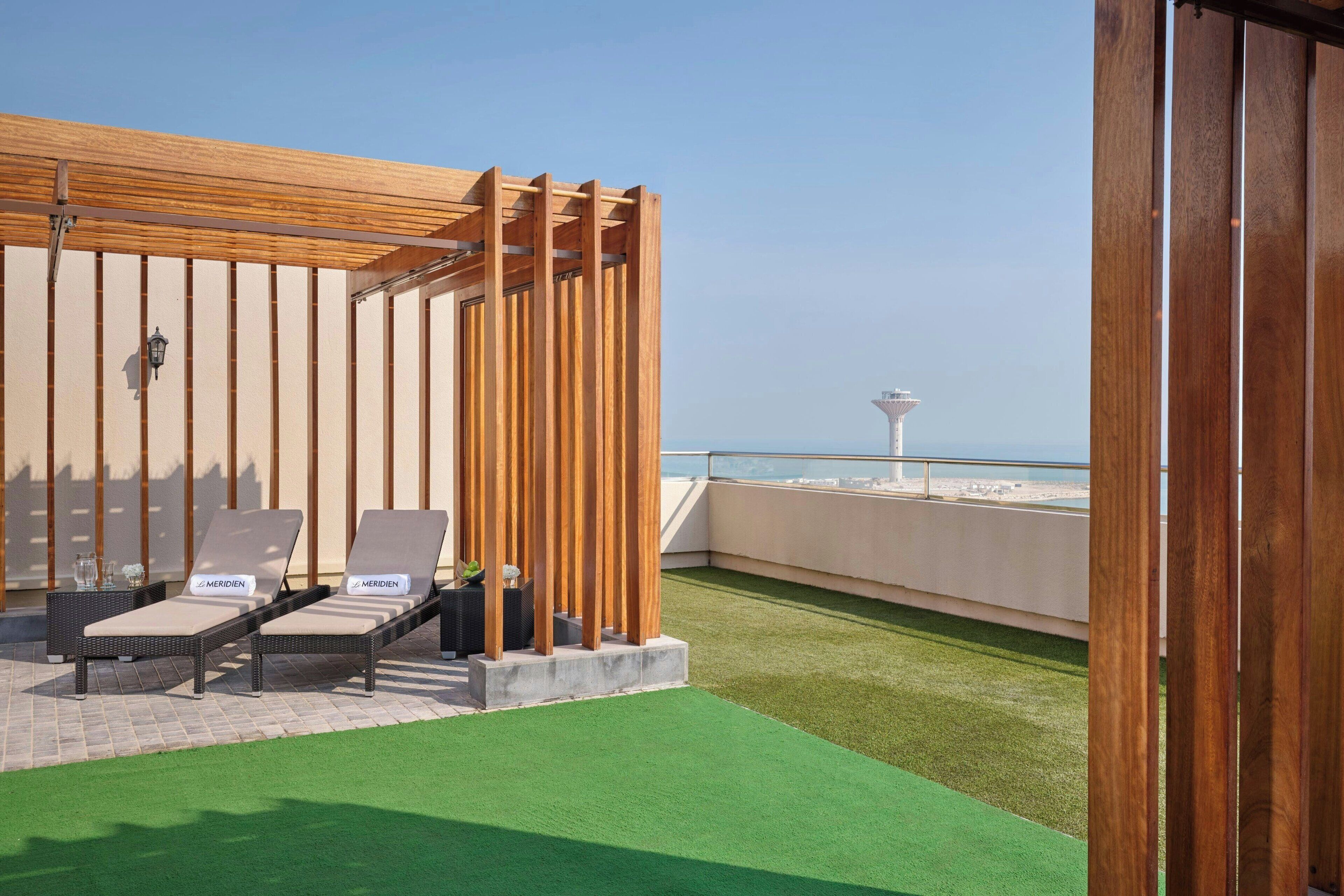 A rooftop terrace with two lounge chairs, a wooden pergola, and a view of the sea.
