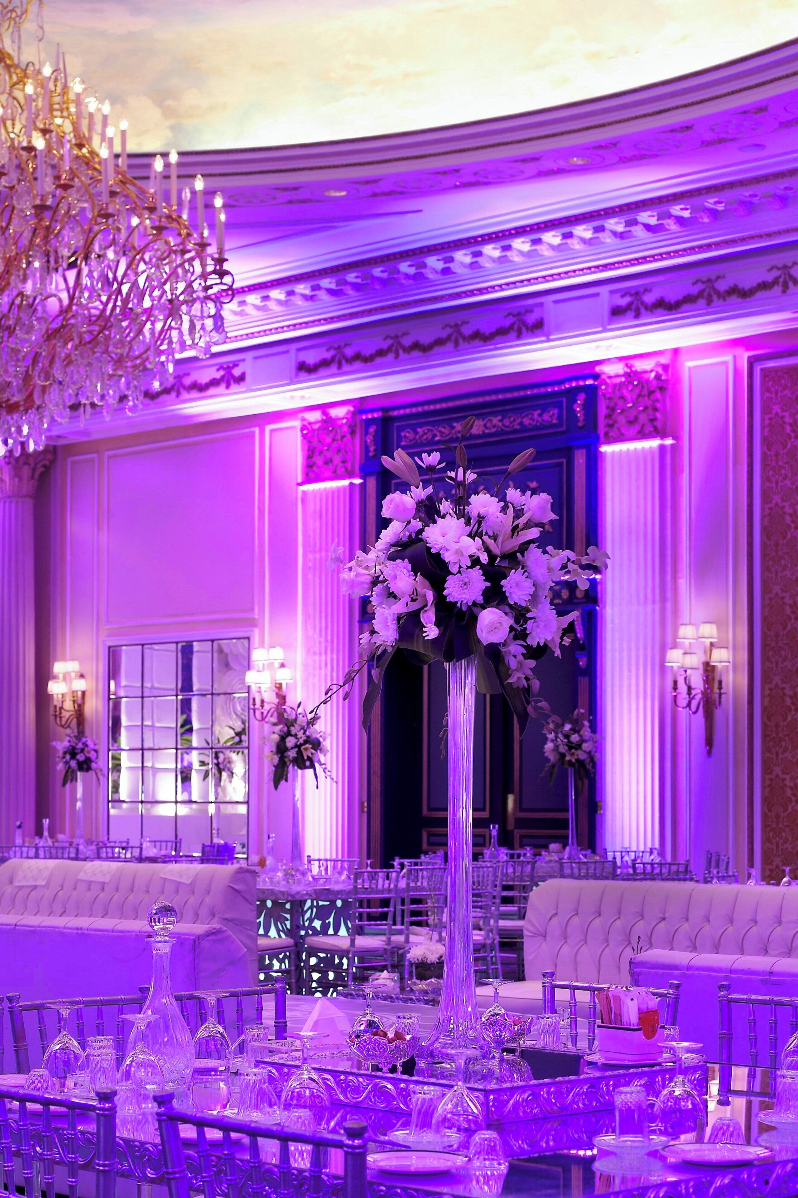 A luxurious dining area with a high-ceiling chandelier, elegant table settings, and a large floral centerpiece.