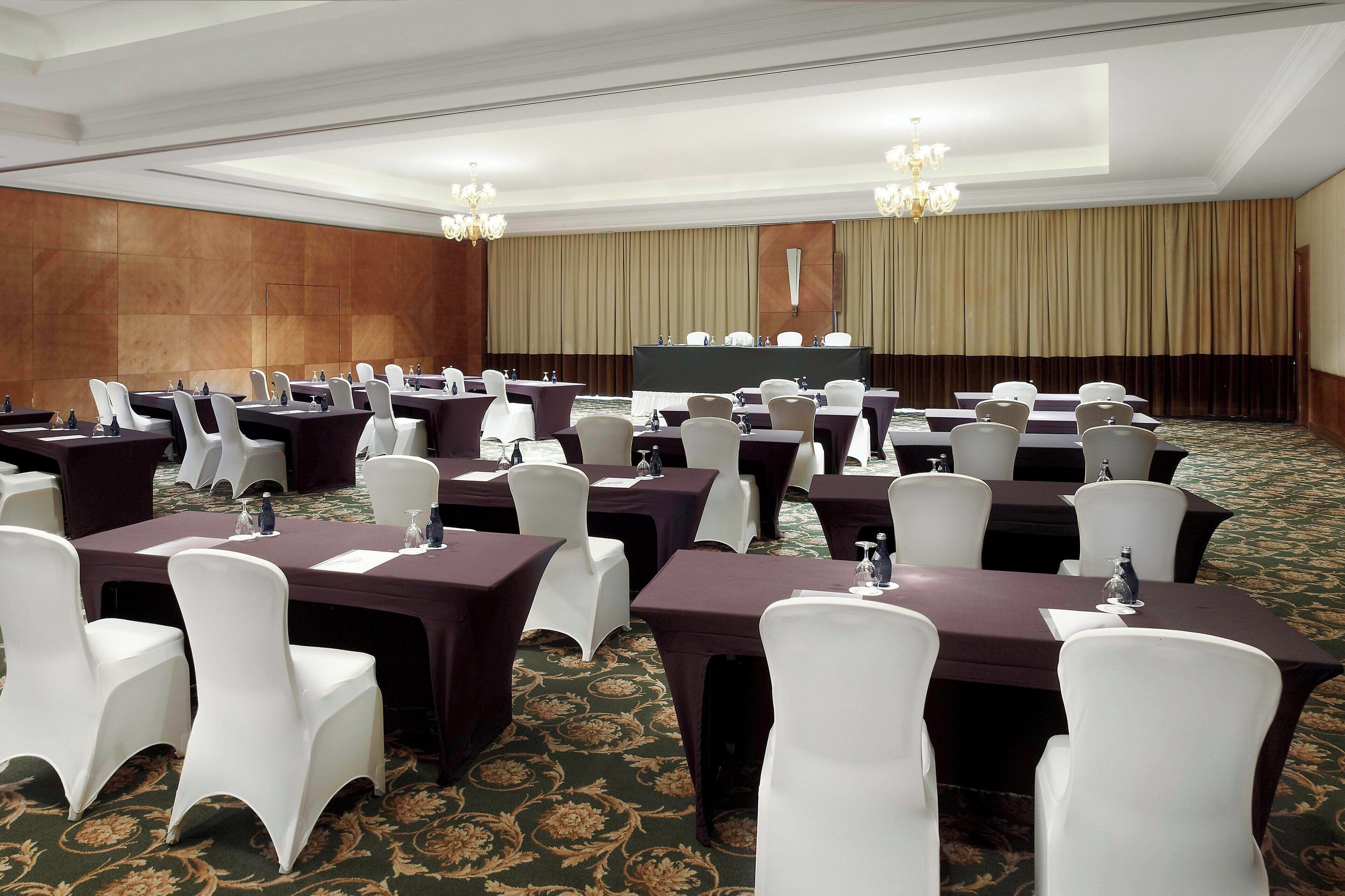 Un salón de conferencias con varias mesas y sillas, una pantalla grande y candelabros.