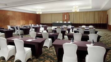 Un salón de conferencias con varias mesas y sillas, una pantalla grande y candelabros.