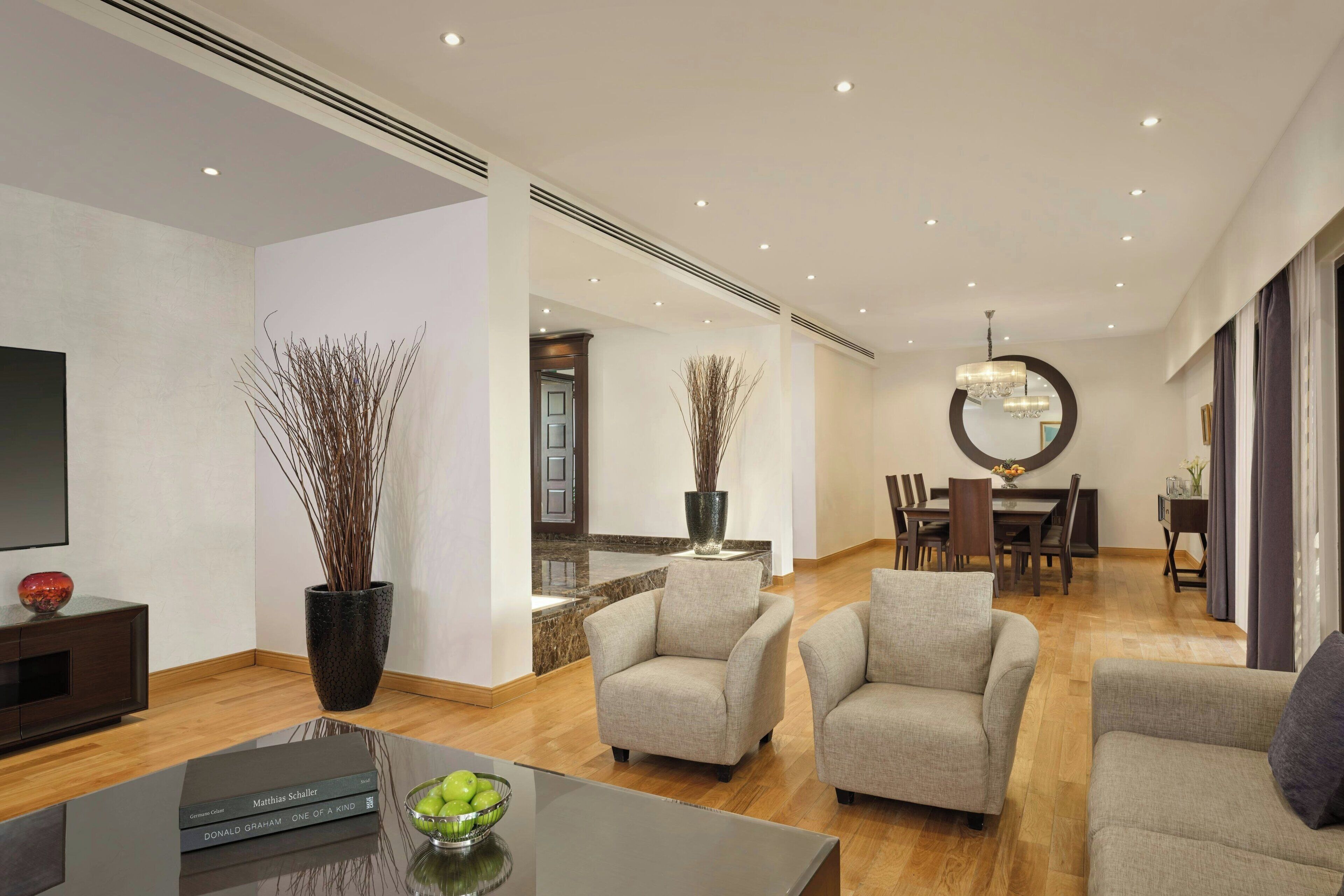 Una sala de estar moderna con un televisor de pantalla plana, una mesa de centro con libros y un frutero, y dos sillones.