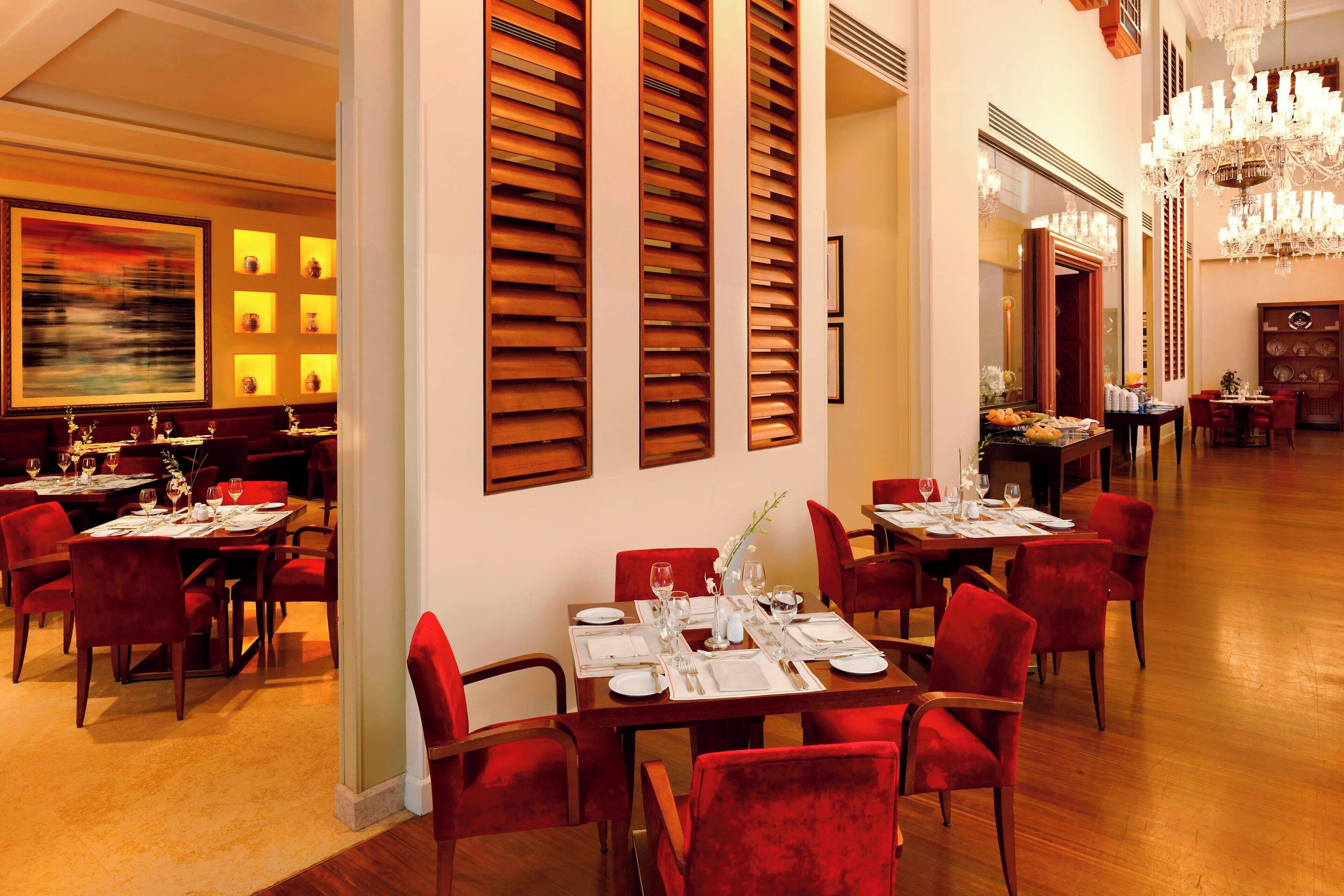 A dining area with tables set for service, red upholstered chairs, and a chandelier.