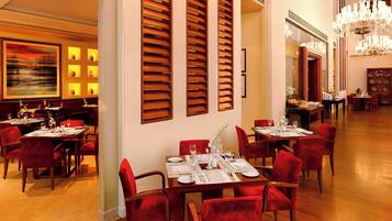 A dining area with tables set for service, red upholstered chairs, and a chandelier.