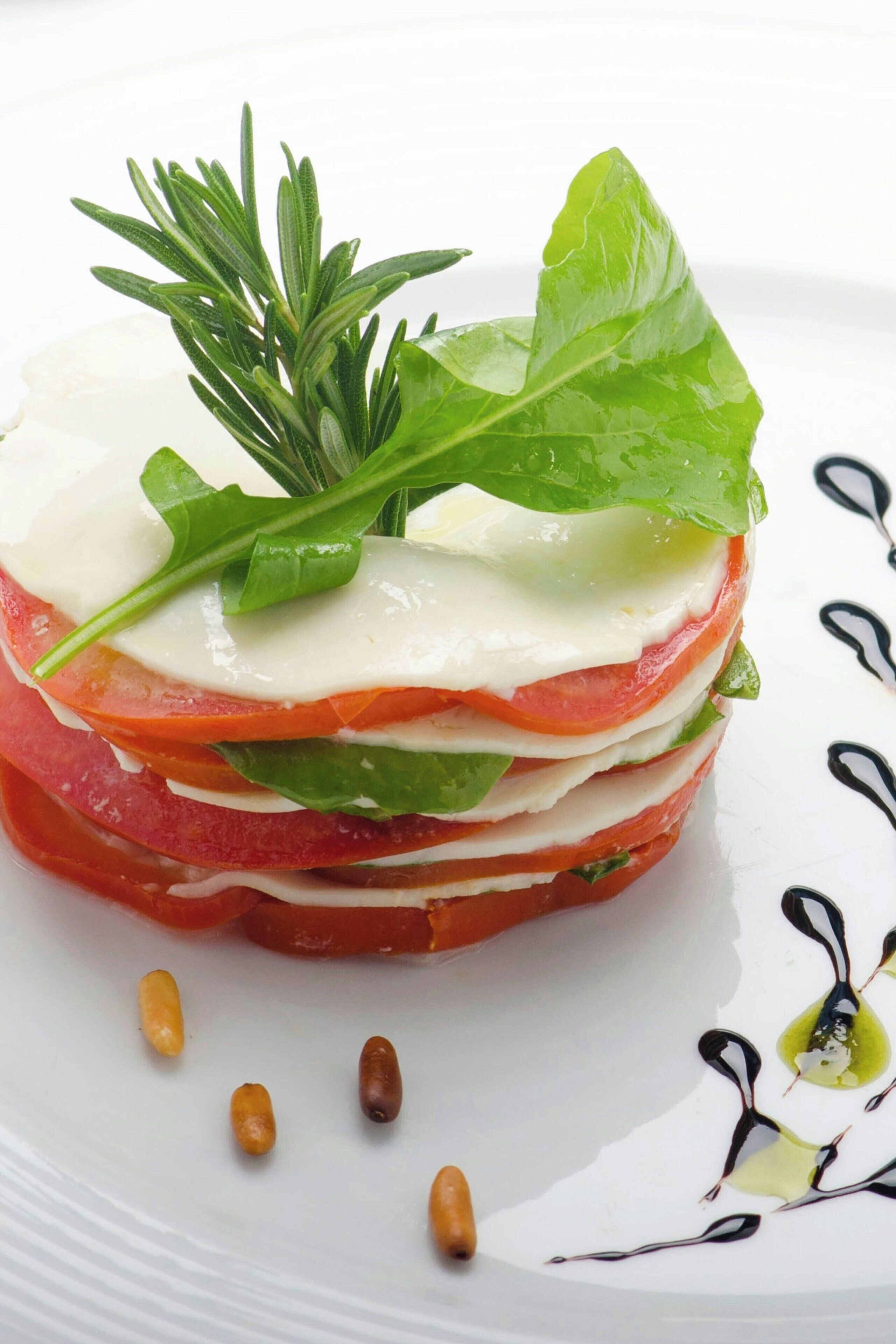 A layered dish with tomatoes, cheese, and greens, garnished with rosemary.