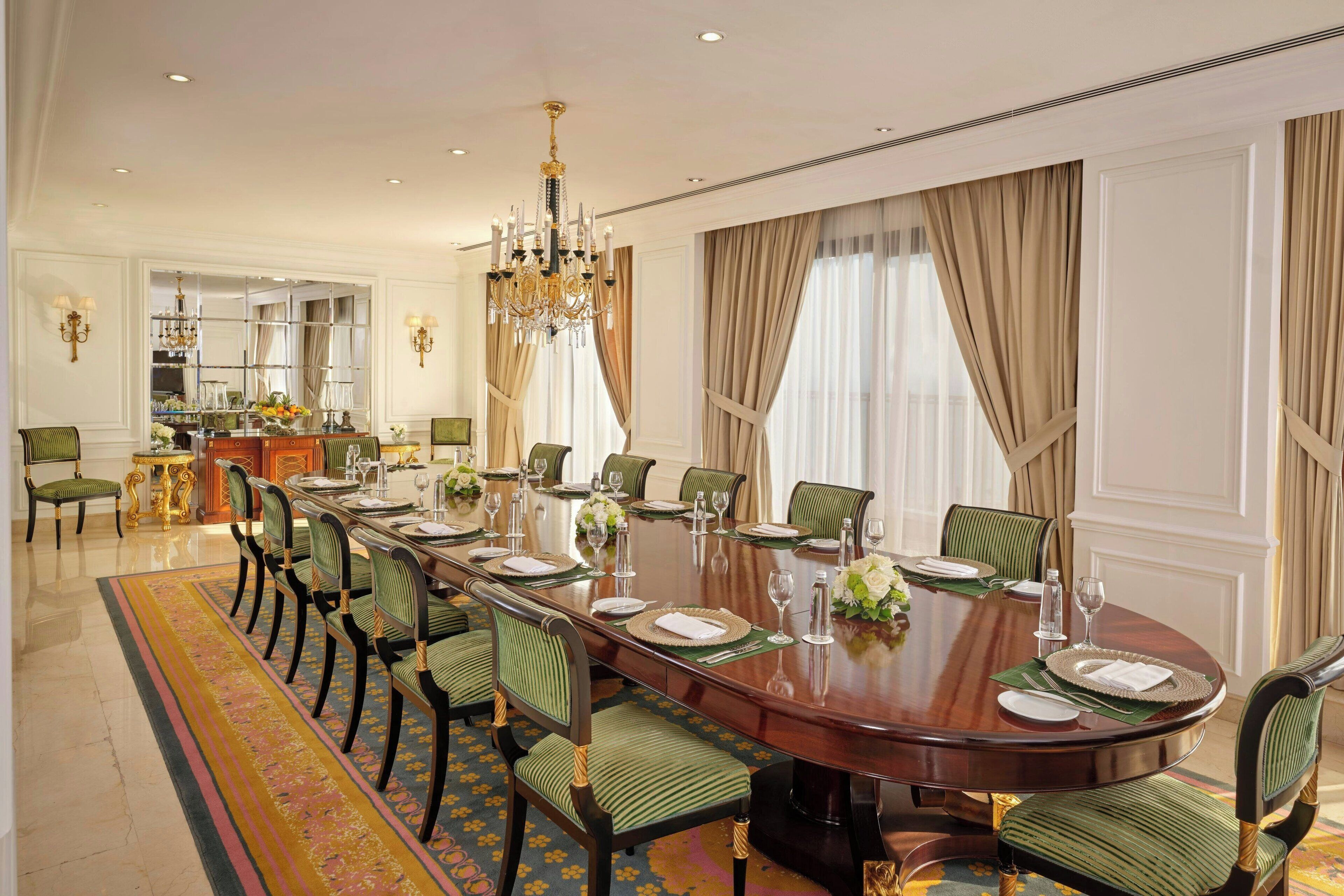 A formal dining room with a long table set for a meal, surrounded by green upholstered chairs.