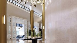 Un vestíbulo moderno con piso reflectante, pilares decorativos y una zona de estar con sillas azules.