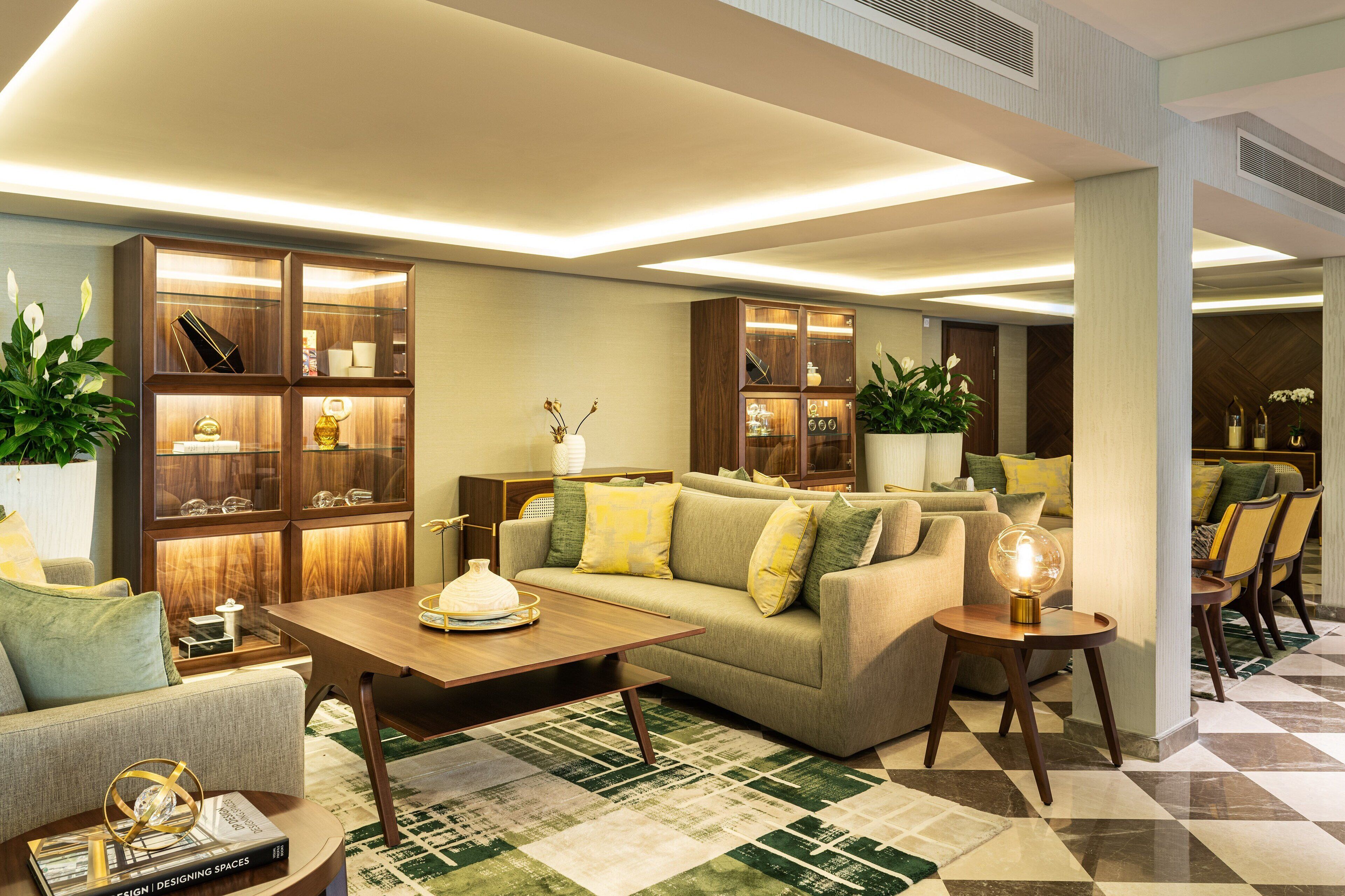 A modern living room with a sofa, coffee table, and books. There is a wooden cabinet with glass doors and a potted plant.
