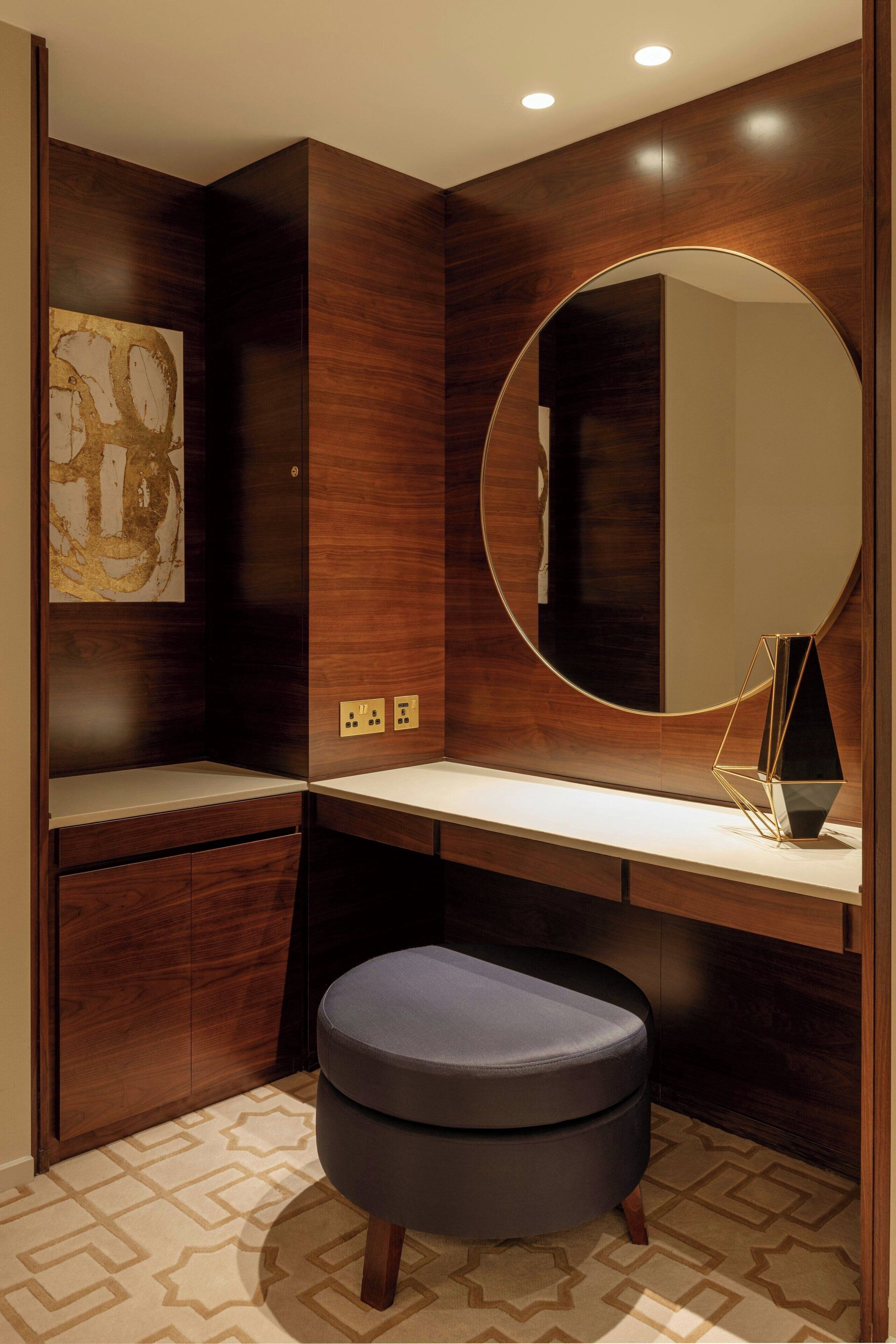 A modern bathroom with a wooden vanity, a round mirror, and a geometric vase on the counter.