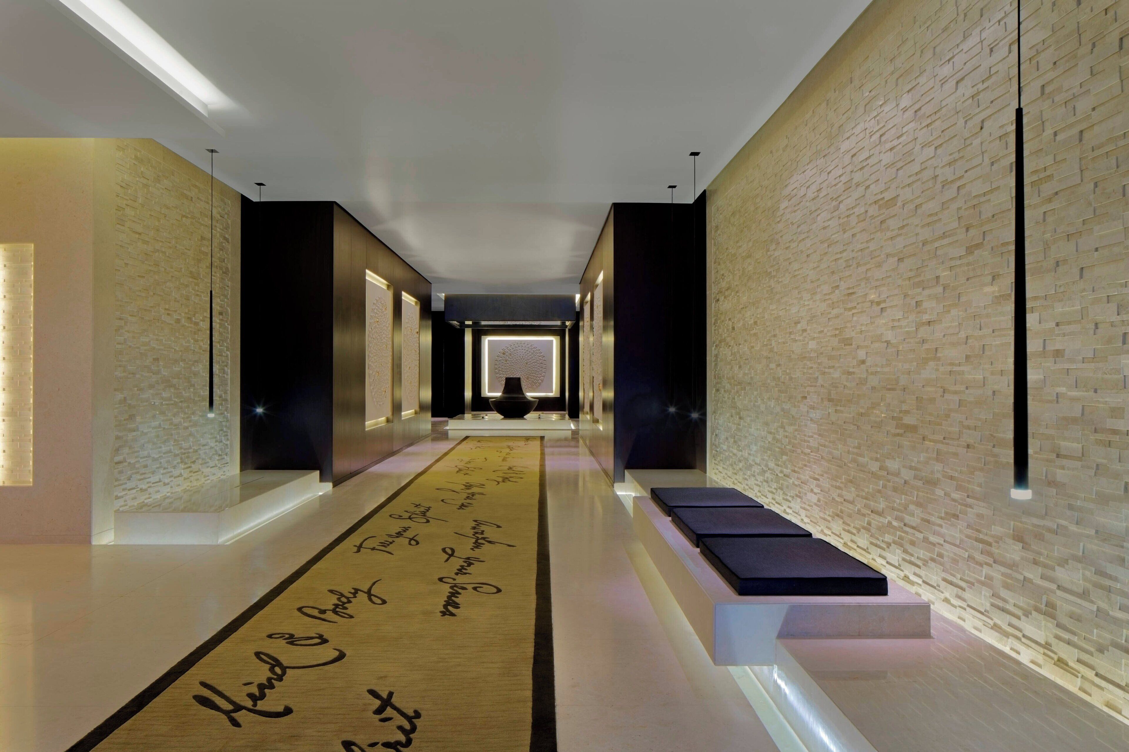 Un couloir moderne avec un long mur éclairé et un tapis décoratif orné de motifs textuels.