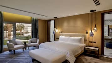 A modern hotel room with a large bed, two armchairs, a small table, and a bench.